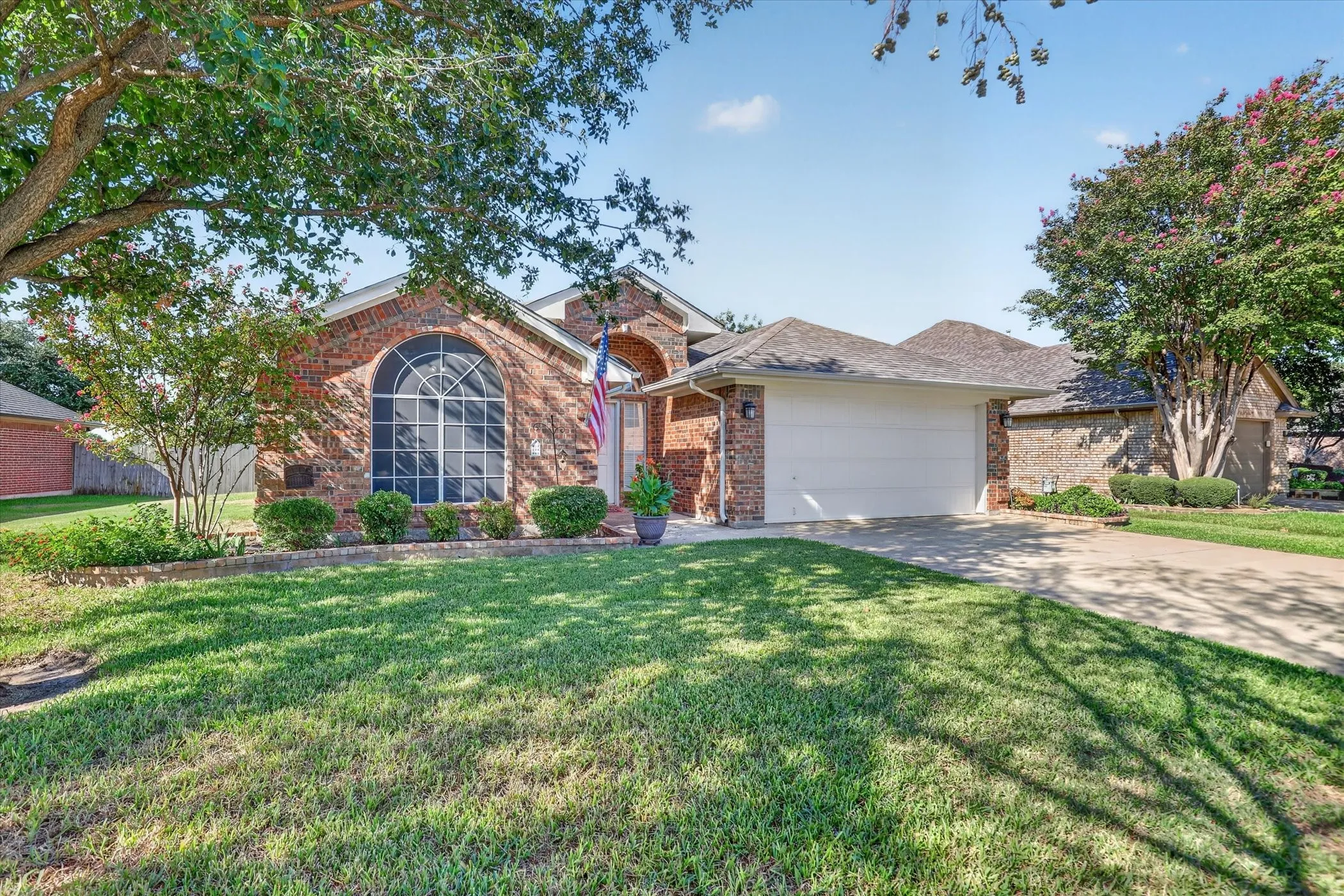 Brick exterior with an arched window, attached garage, and concrete driveway