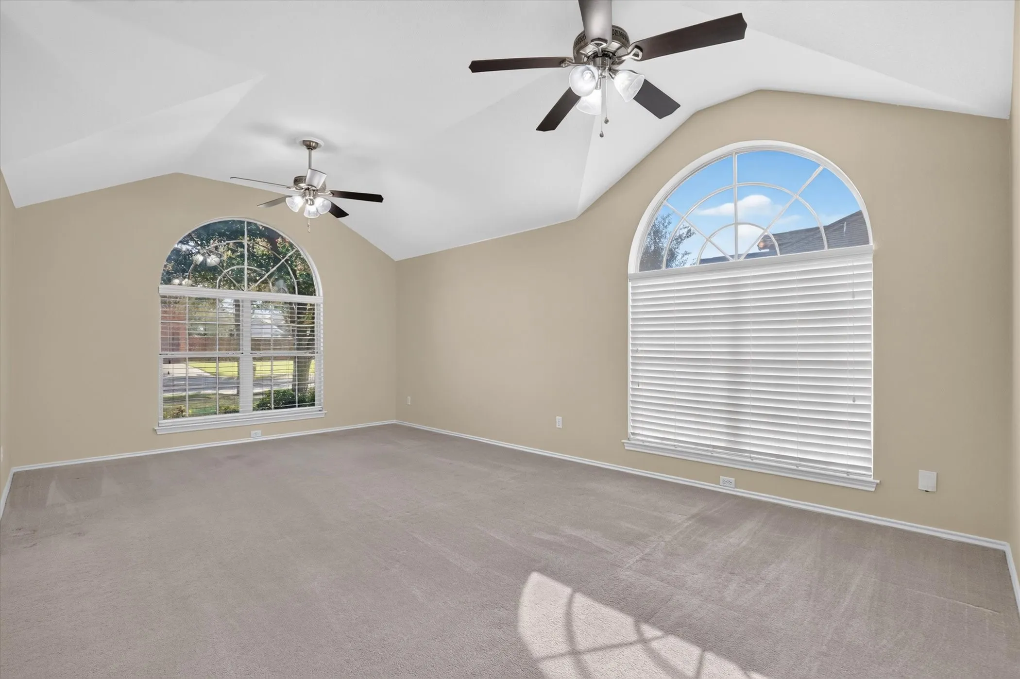 Vaulted ceilings with two ceiling fans, two large arched windows, and light beige carpet
