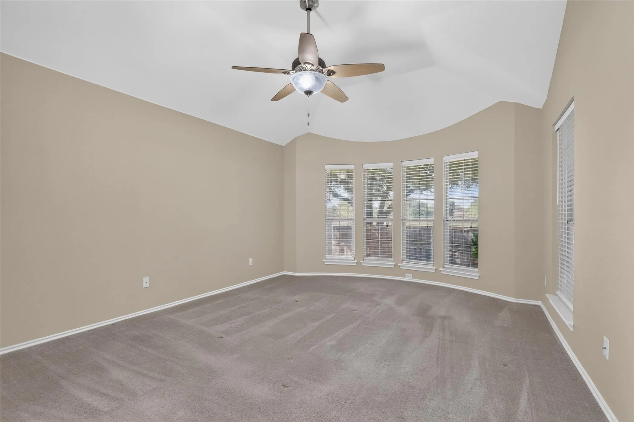 Spacious room with vaulted ceiling and ceiling fan, neutral wall finishes, and expansive multi-pane windows providing natural light