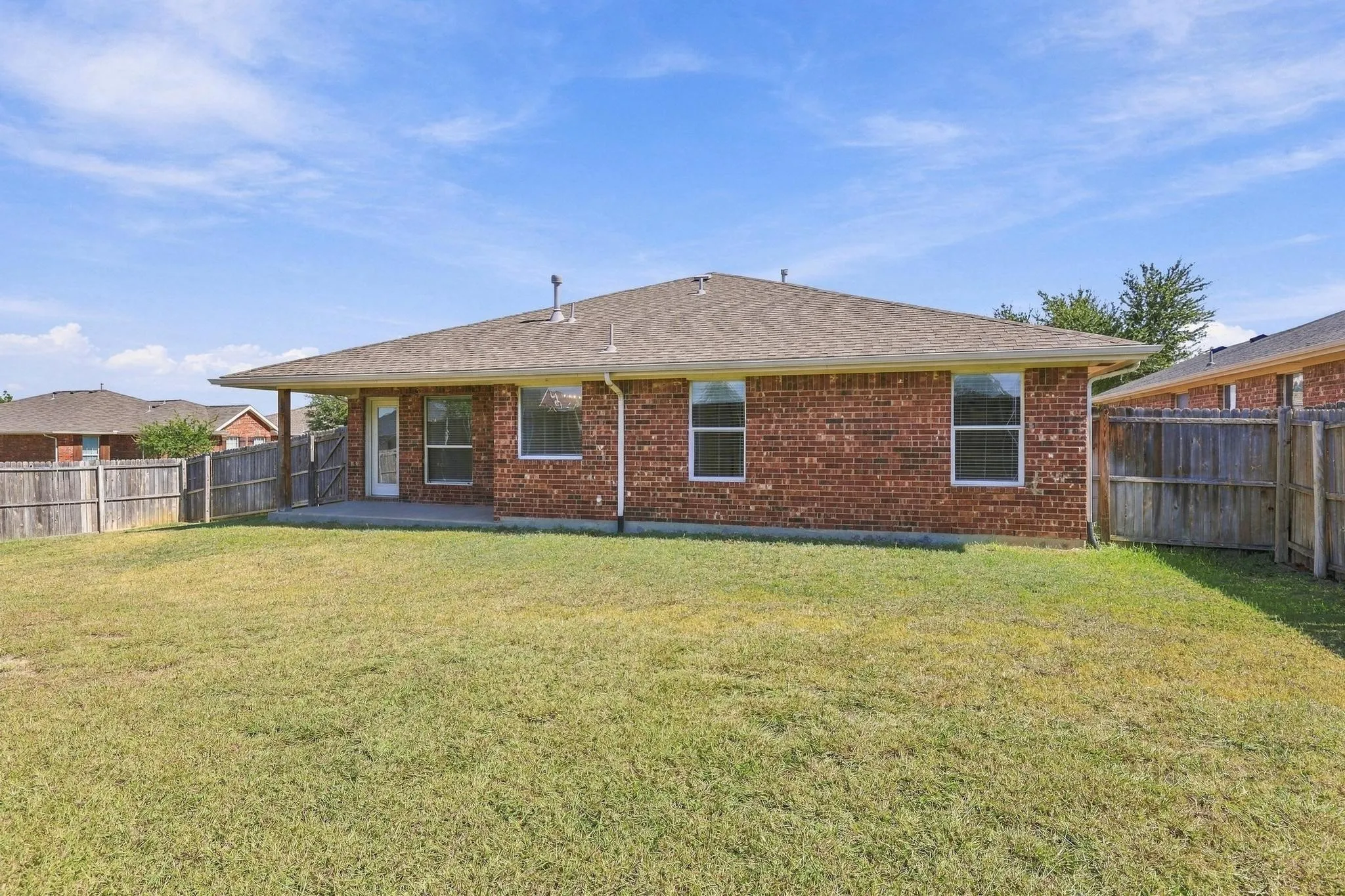 Expansive backyard with a manicured lawn, full brick exterior, and a covered patio area