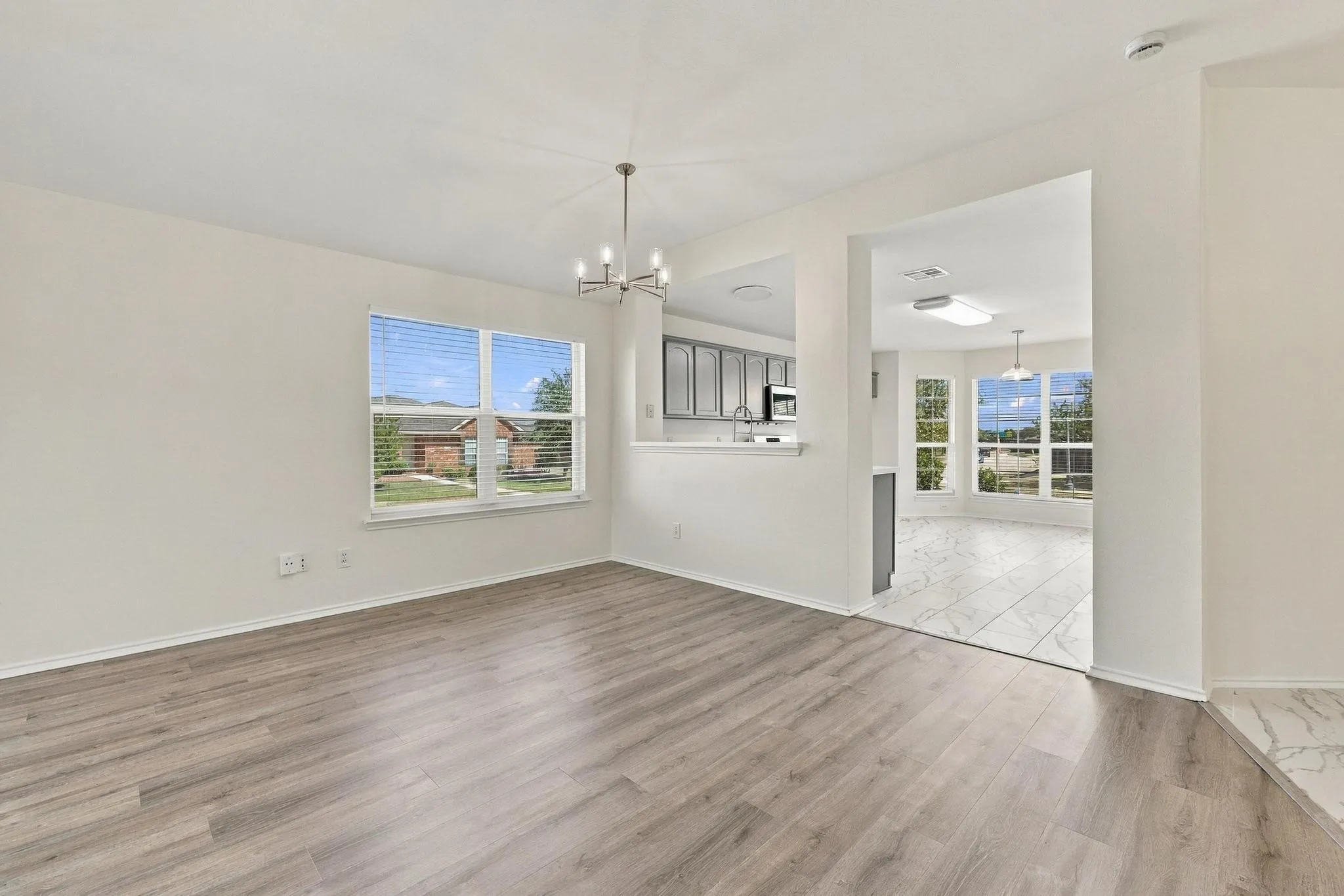 Wood-finish flooring, contemporary chandelier, double windows with blinds, built-in kitchen cabinetry, and large format floor tile