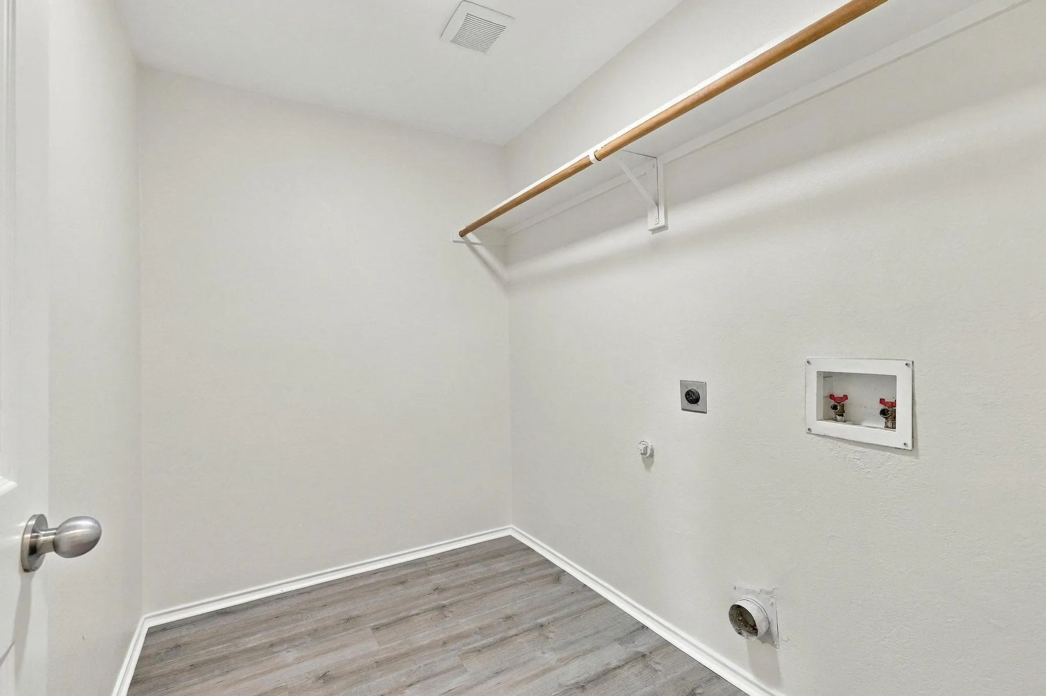Laundry area featuring wood-finish flooring, a wall-mounted clothing rod, and visible utility connections