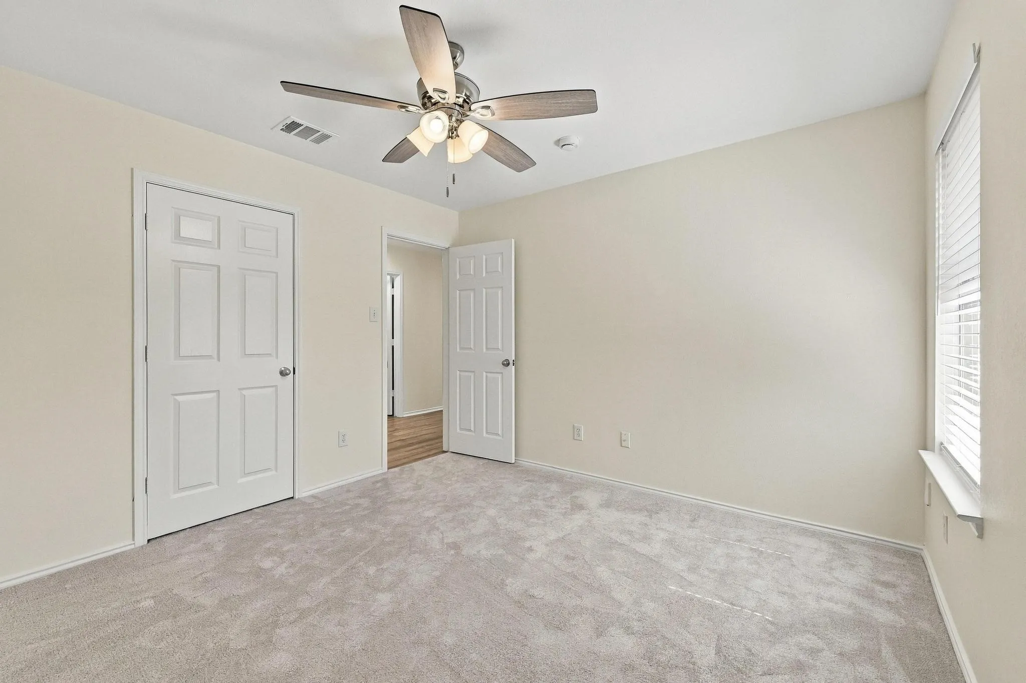 Carpeted room with a ceiling fan, paneled doors, and a window with blinds