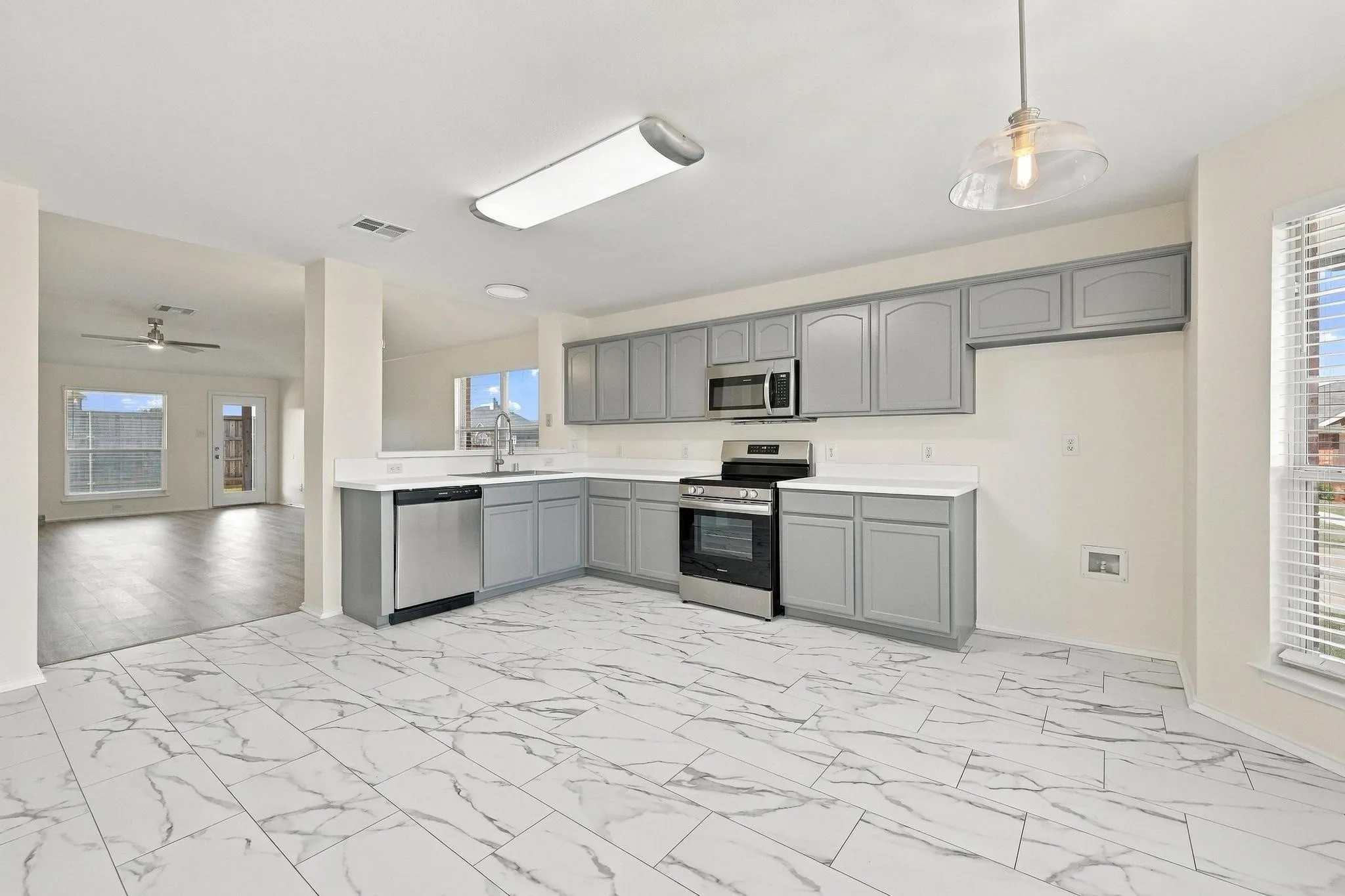 Kitchen featuring L-shaped gray cabinetry, stainless steel appliances, a stainless steel sink, and white countertops
