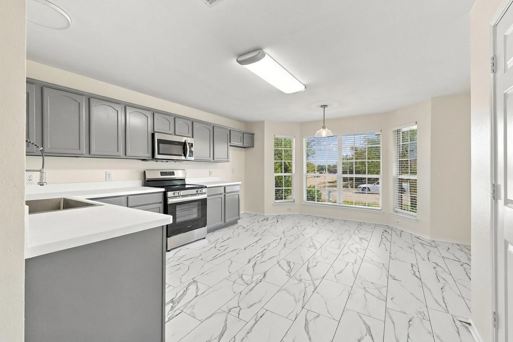 Kitchen featuring gray cabinetry, stainless steel appliances, white countertops, and marble-look tile flooring