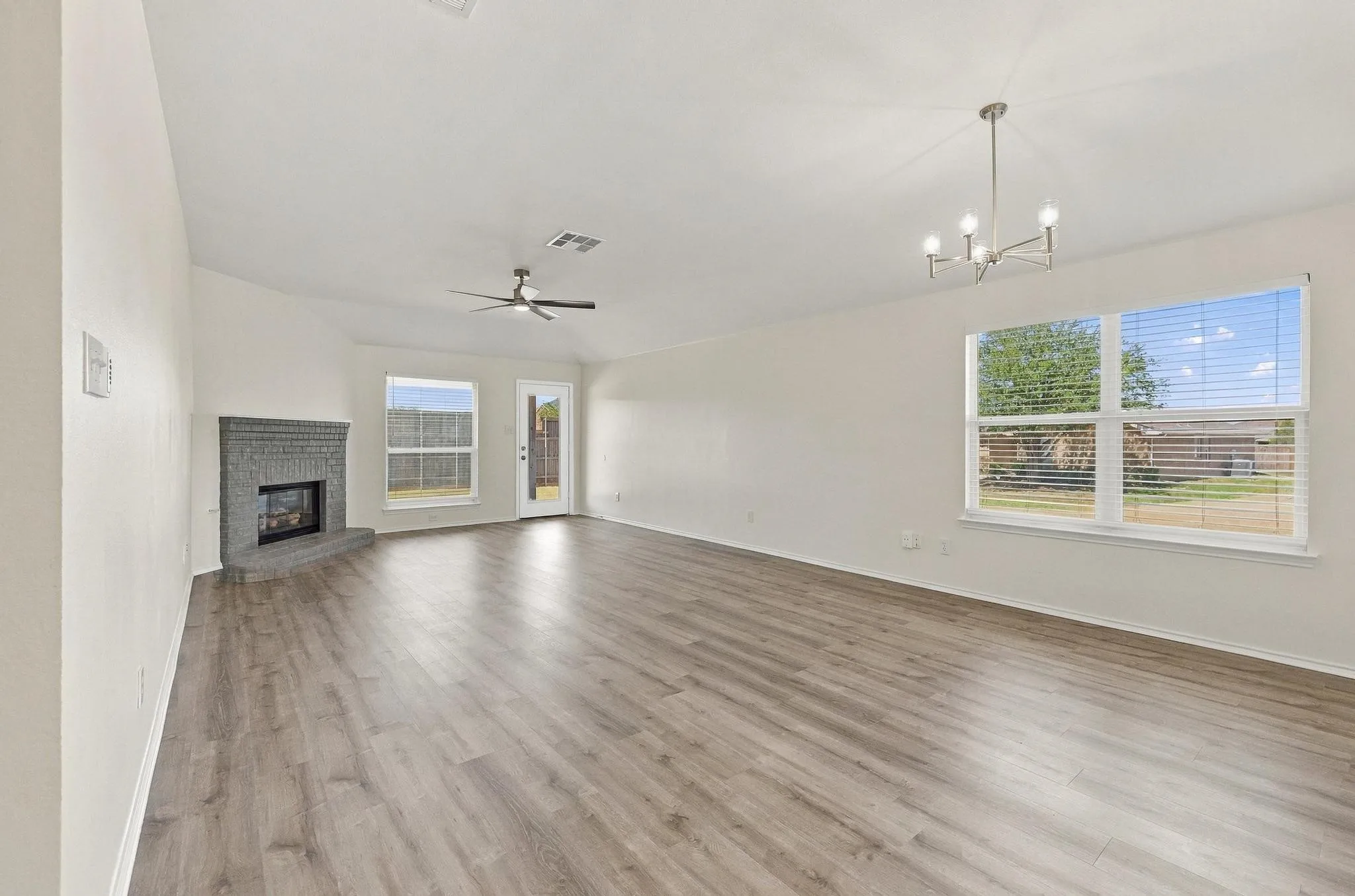 Spacious living area featuring wood-finish flooring, a contemporary chandelier, and a ceiling fan