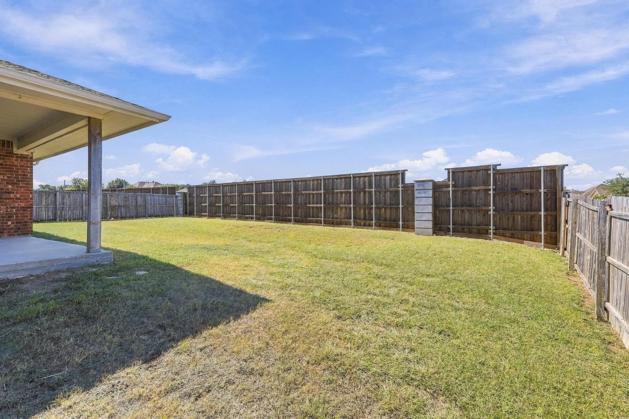 Expansive grassy yard with wood privacy fencing and an exterior patio