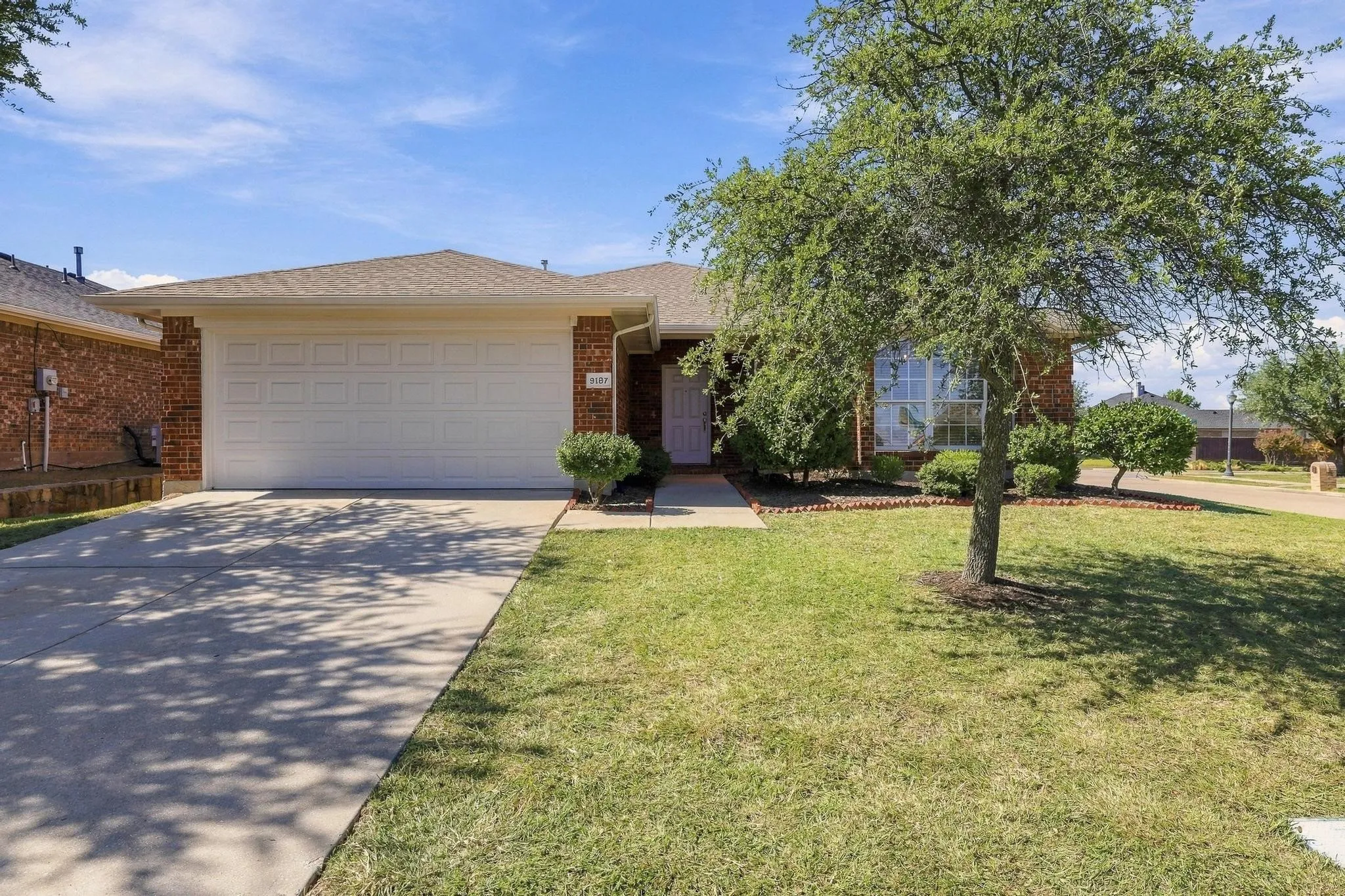 Brick exterior with a white garage door, concrete driveway, and front lawn