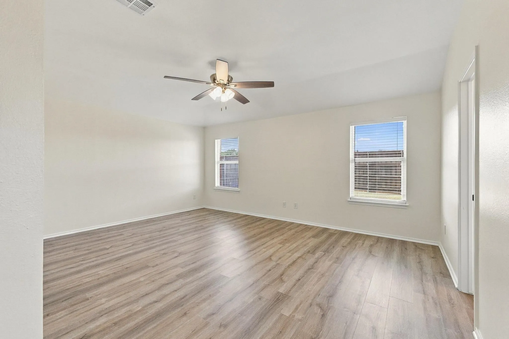 Spacious room featuring wood-finish flooring, two windows with blinds, and a ceiling fan