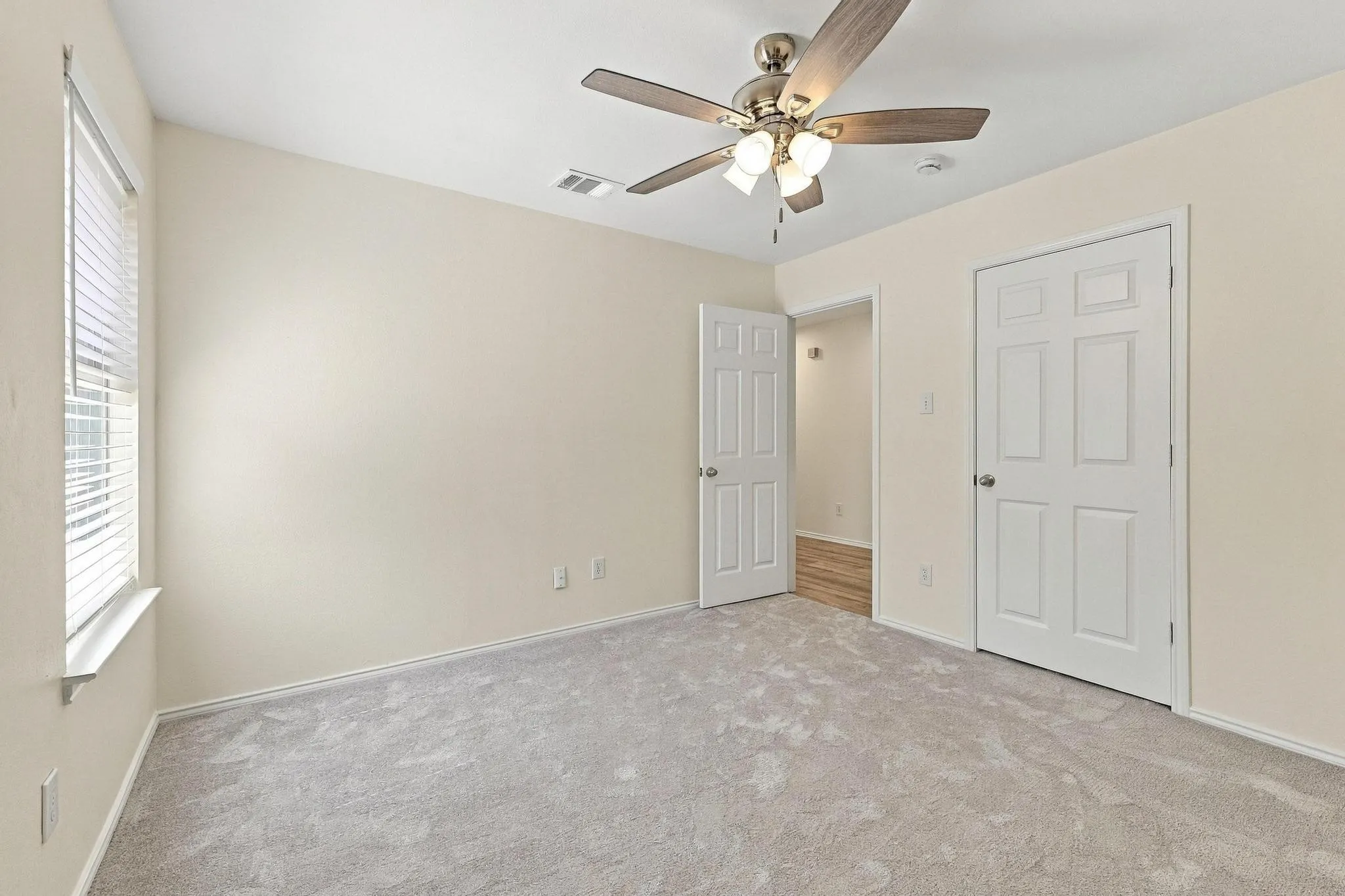 Plush carpet flooring, neutral paint palette, ceiling fan with integrated lighting, white paneled doors, and window with blinds