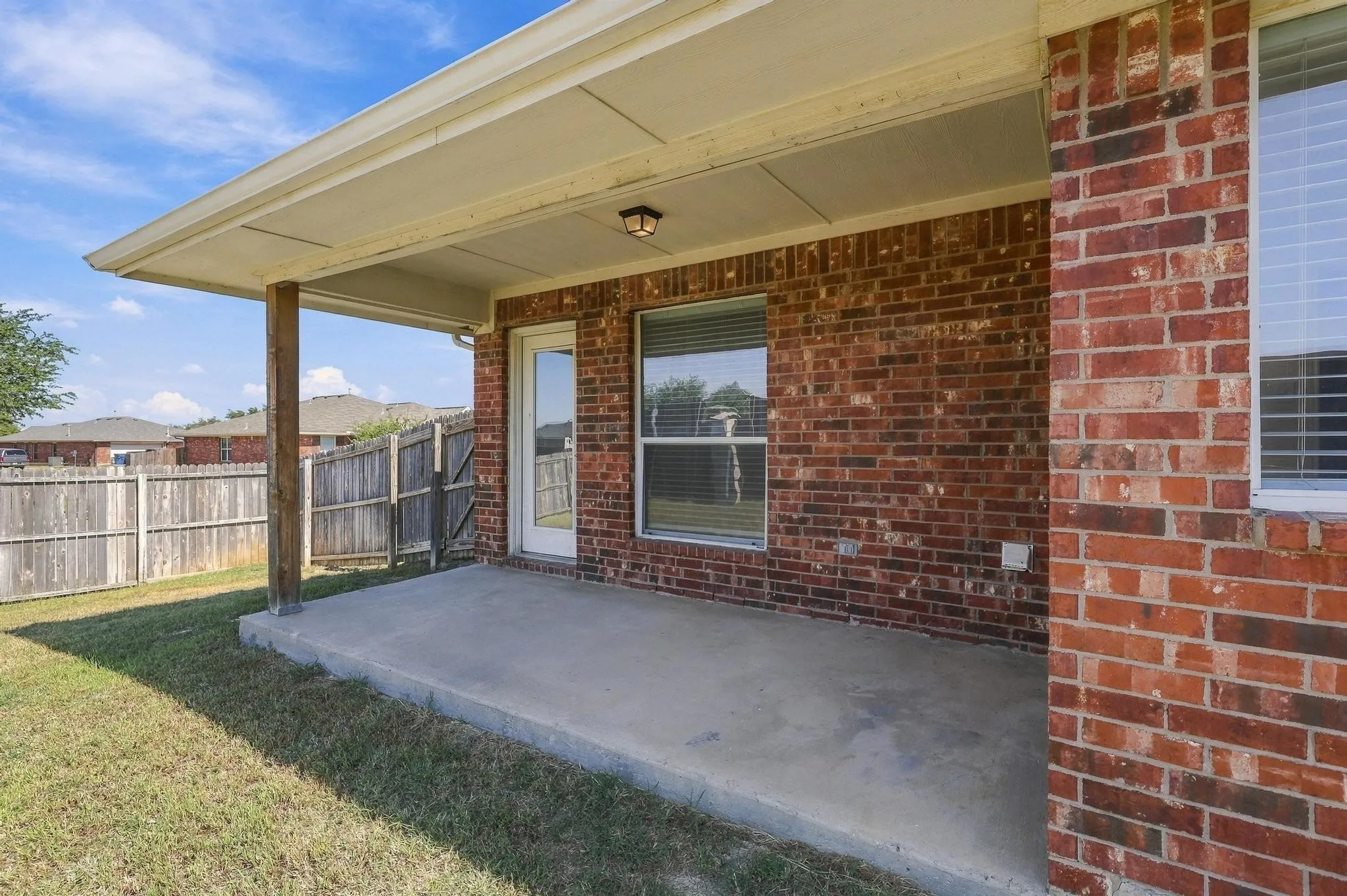Covered patio with a concrete slab, brick exterior, and a wood privacy fence