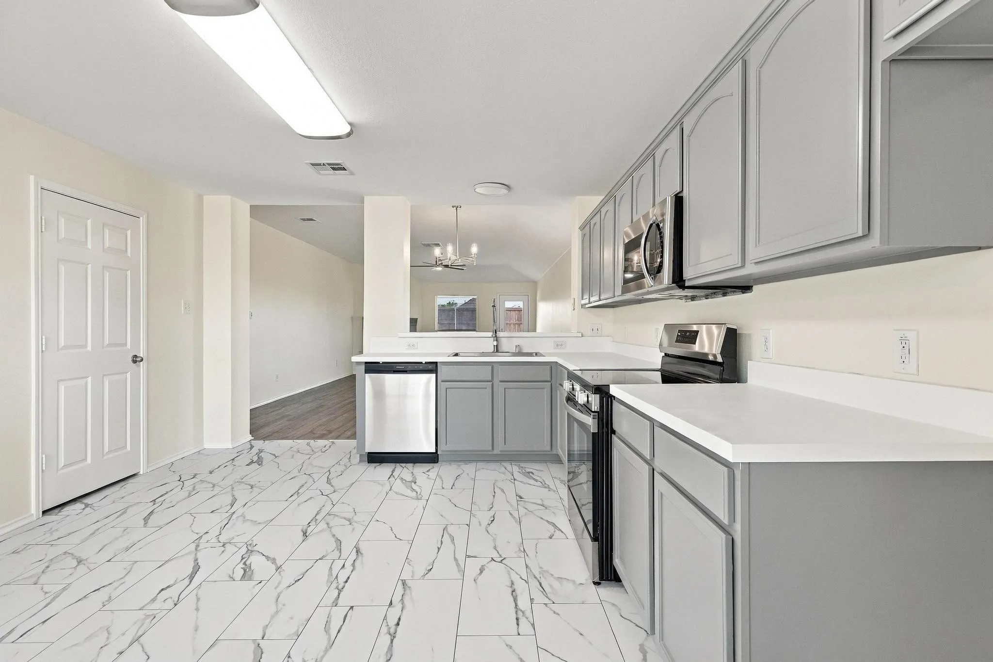 Kitchen featuring light grey cabinetry, white countertops, stainless steel appliances, and large format marble-look floor tiles