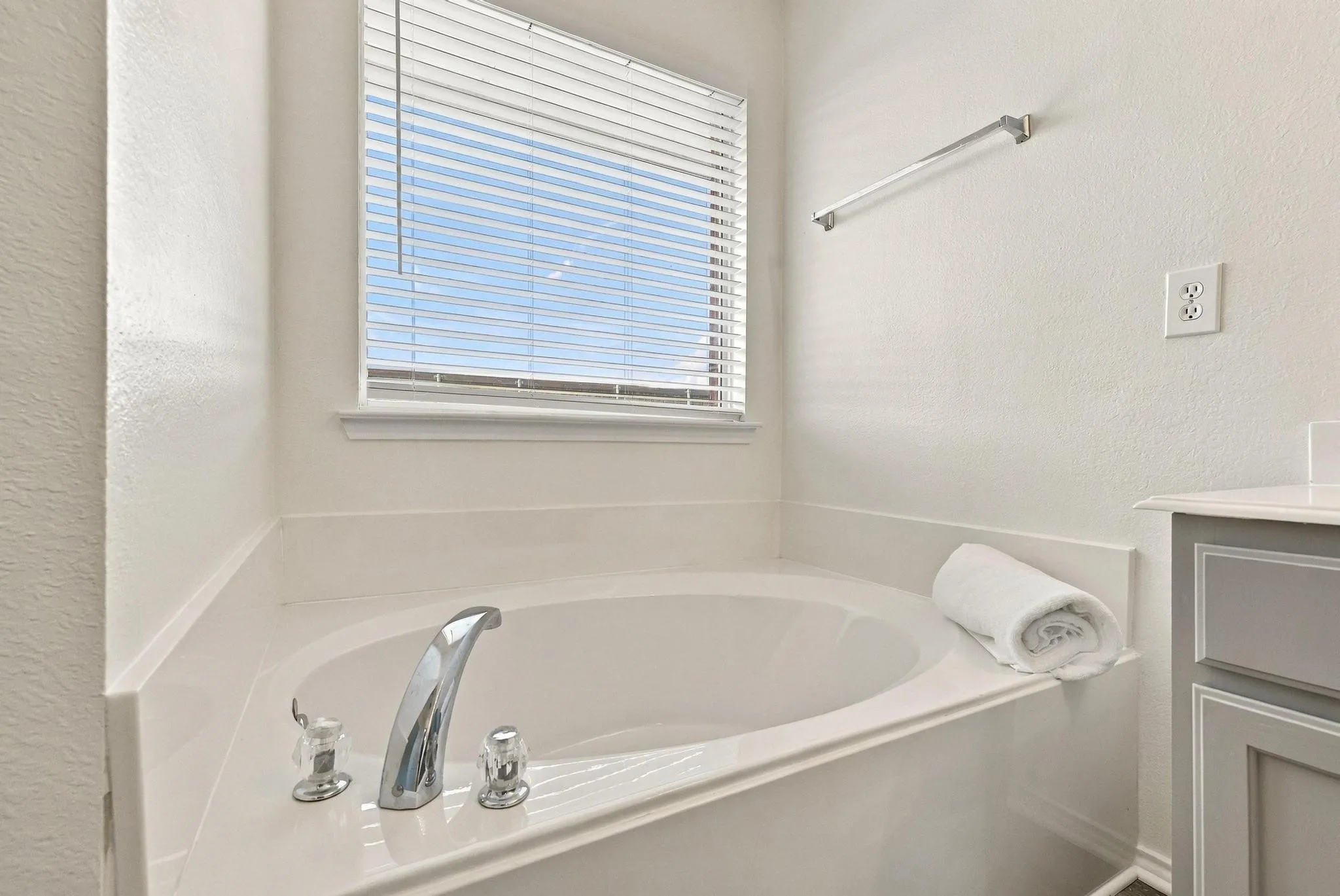 Alcove soaking tub with chrome fixtures, integrated white countertop, and window with horizontal blinds