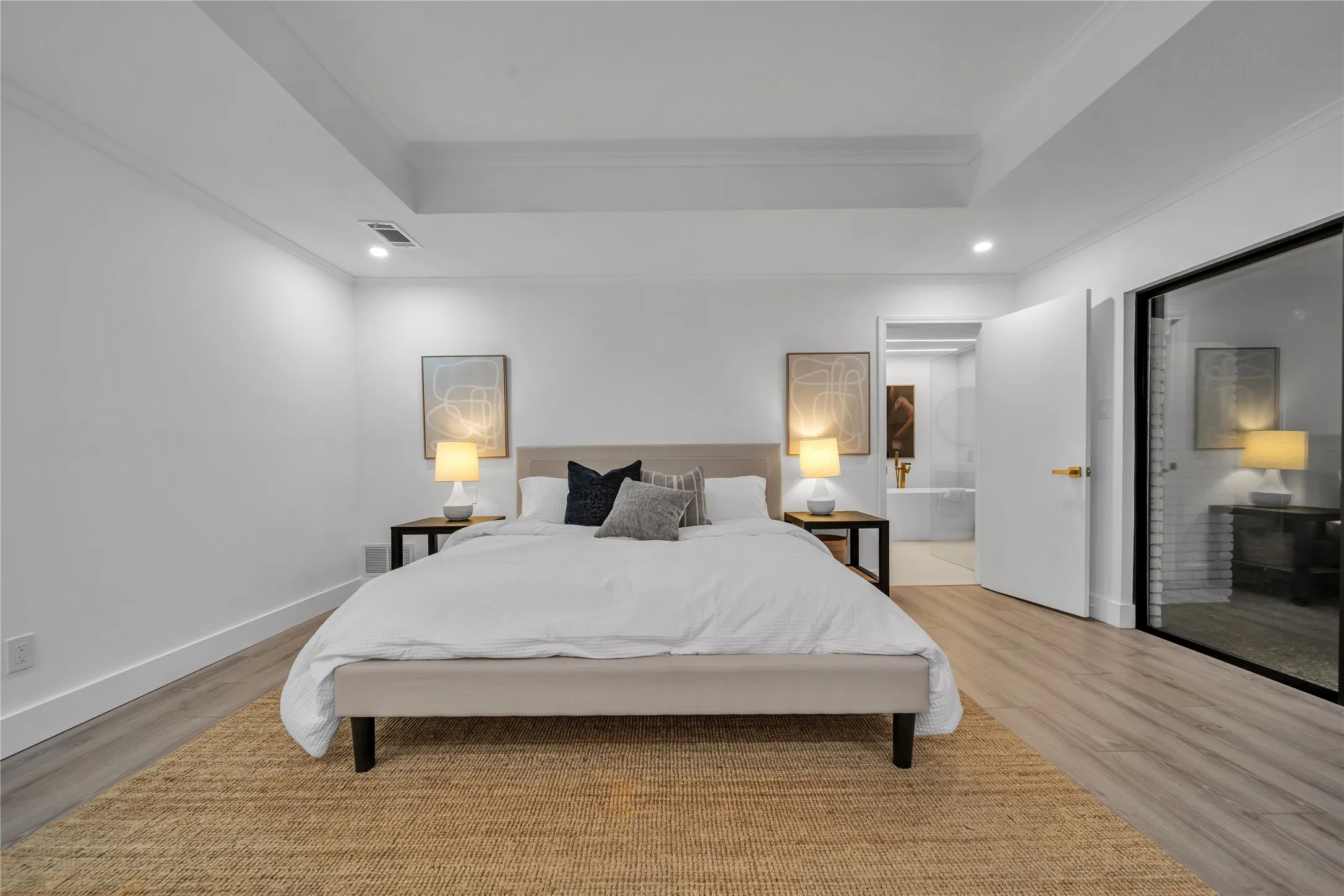 Bedroom featuring a raised ceiling, light wood-type flooring, ensuite bath, and ornamental molding