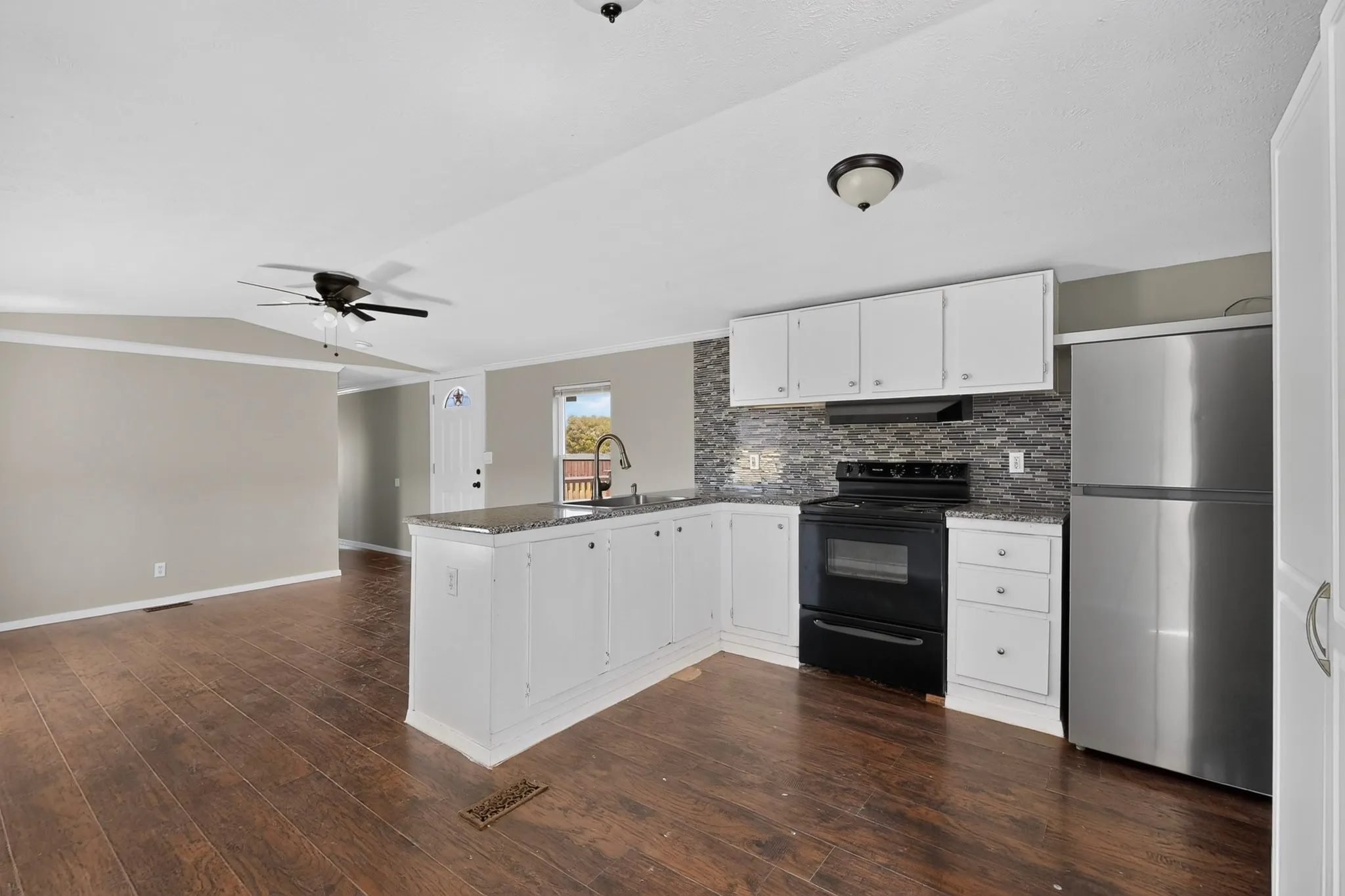 Wood-finish flooring throughout, white cabinetry, dark stone countertops, mosaic tile backsplash, and stainless steel refrigerator