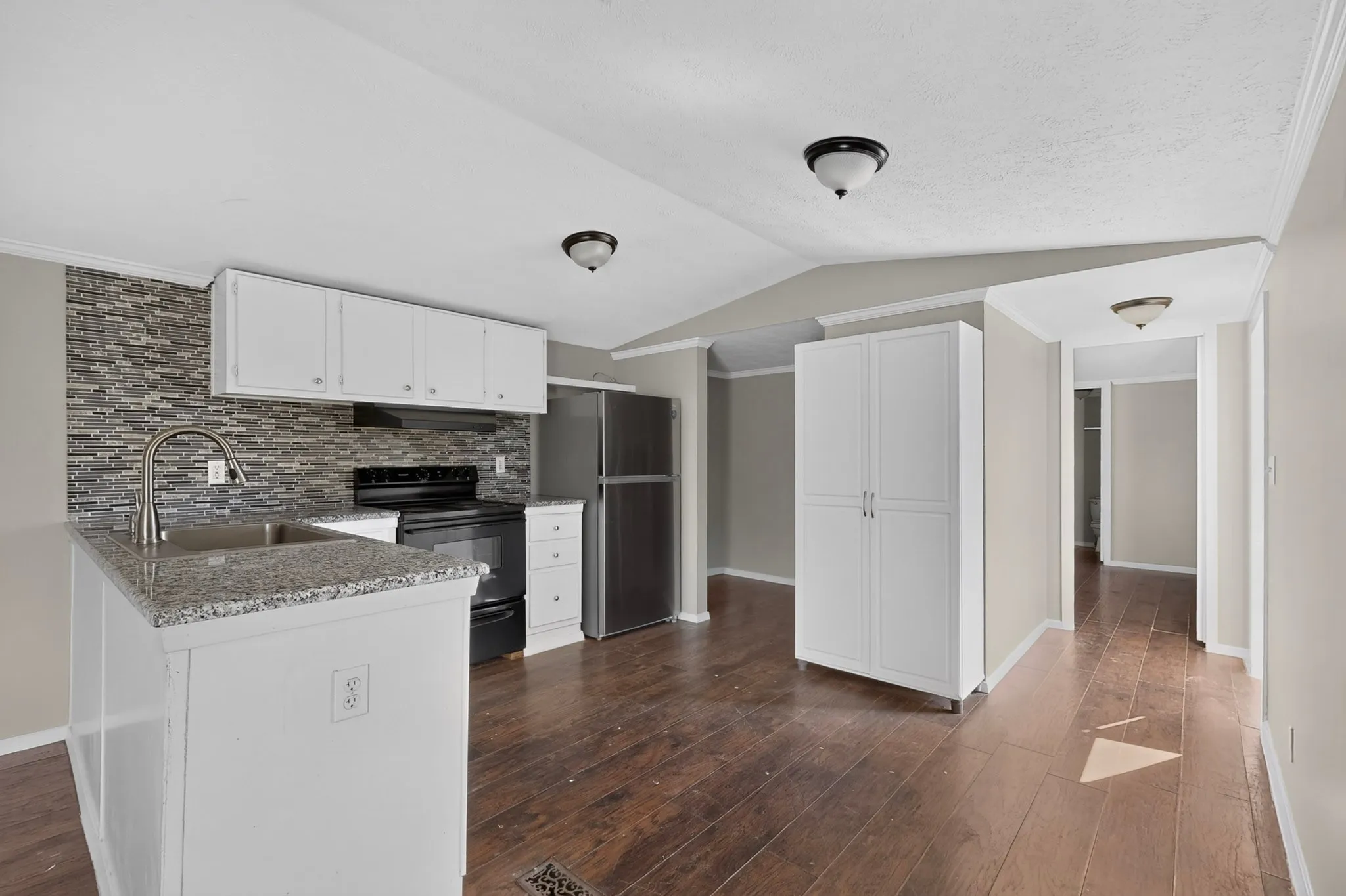Kitchen featuring wood-finish flooring, white cabinetry, granite-style countertops, mosaic tile backsplash, and stainless steel appliances