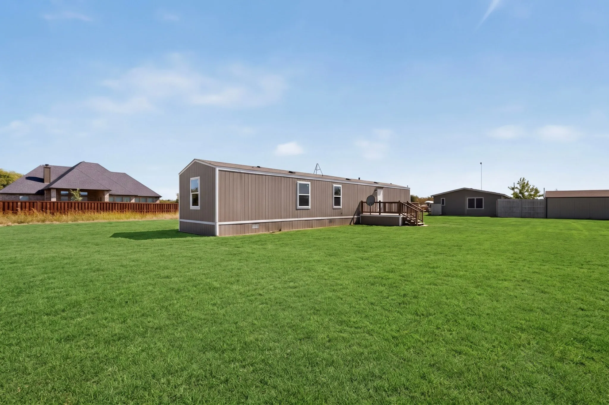 Expansive green lawn, brown siding, multiple windows, wooden deck, wooden steps
