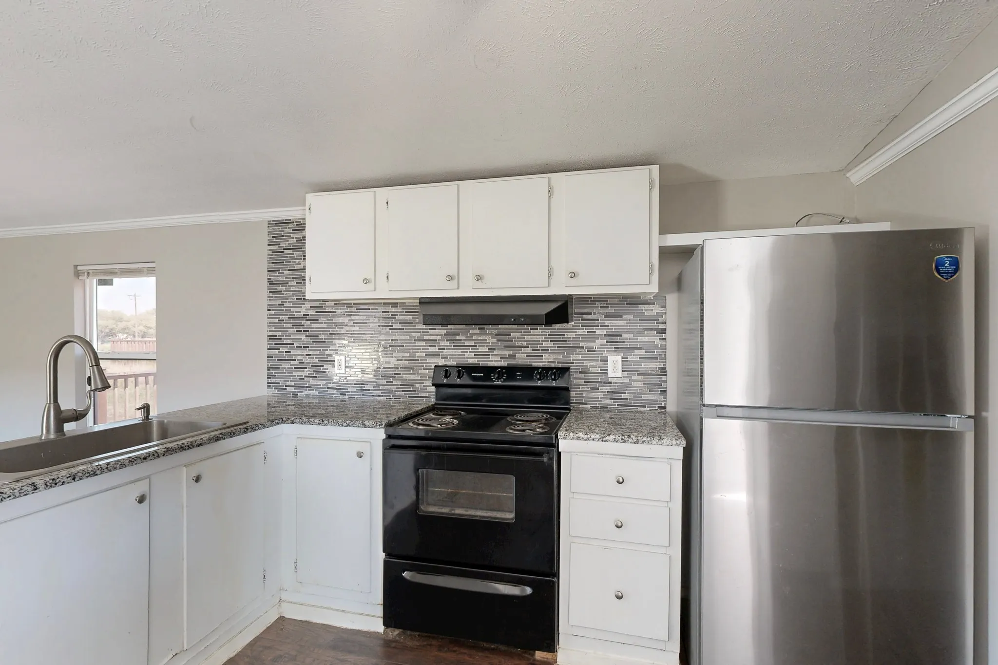 White cabinetry with chrome hardware, tile backsplash, black electric range, stainless steel refrigerator, and a stainless steel sink with a gooseneck faucet