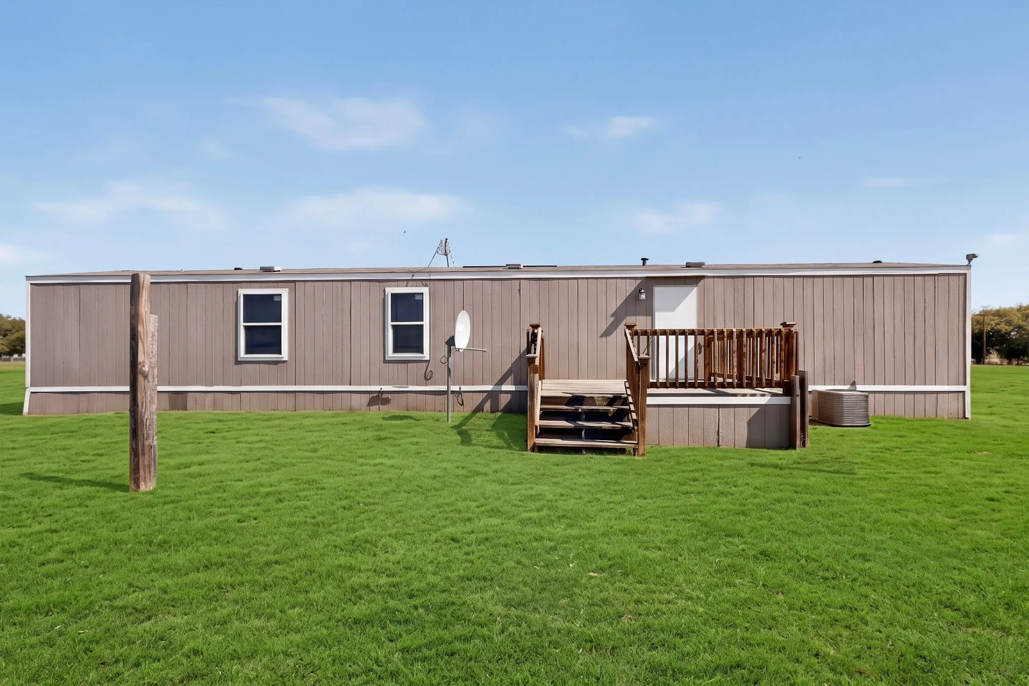 Expansive green lawn, wood-finish exterior siding, white frame windows, wood deck with railings, and a white entry door
