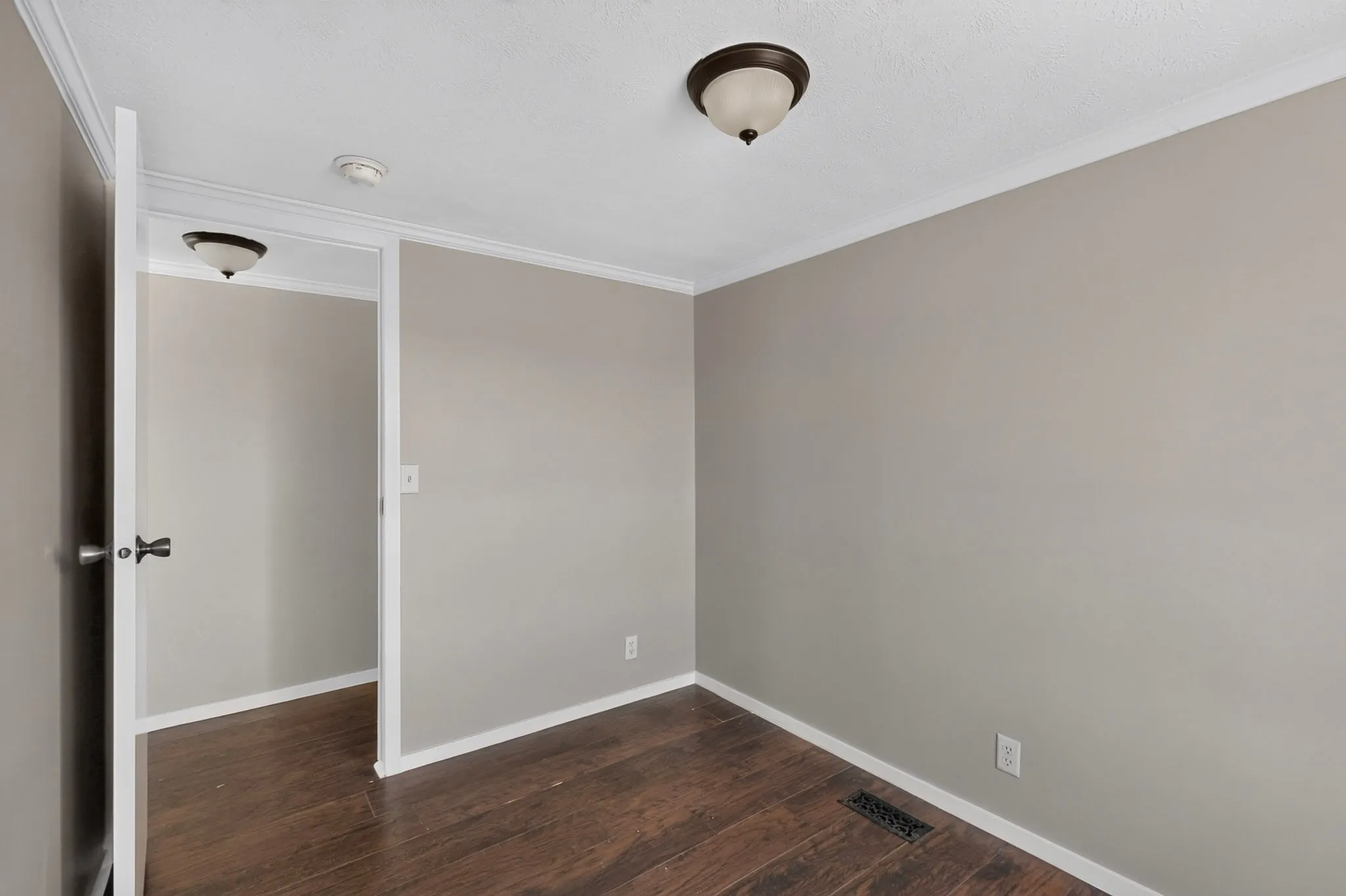Bright secondary bedroom featuring neutral wall finishes, wood-finish flooring, white trim detailing, and dual ceiling-mounted light fixtures