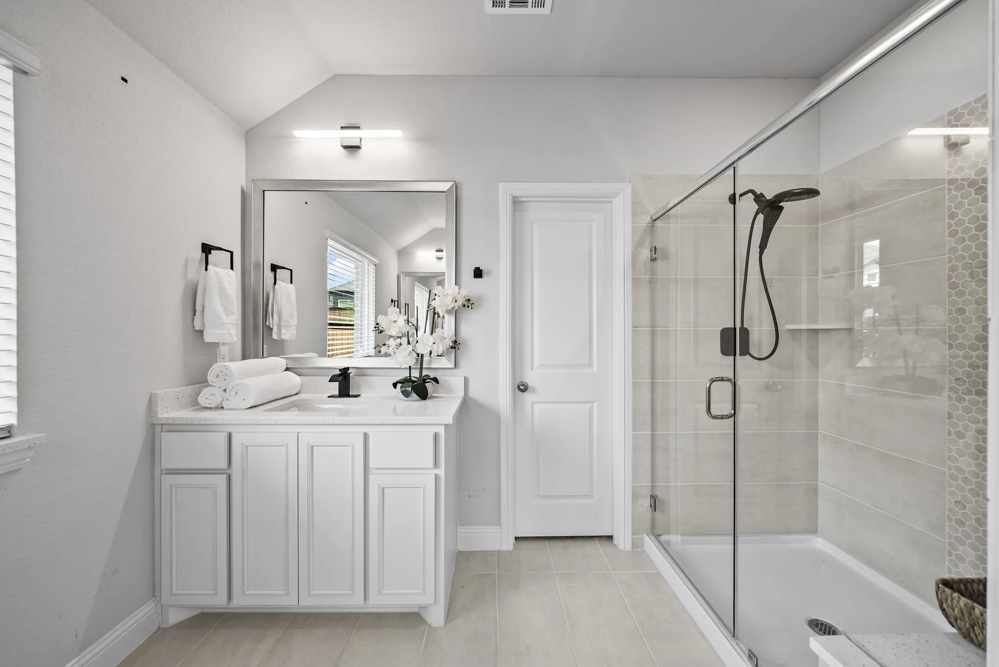 Walk-in shower with clear glass enclosure and light-toned tile, single vanity with white cabinetry, light-toned countertop, and undermount sink