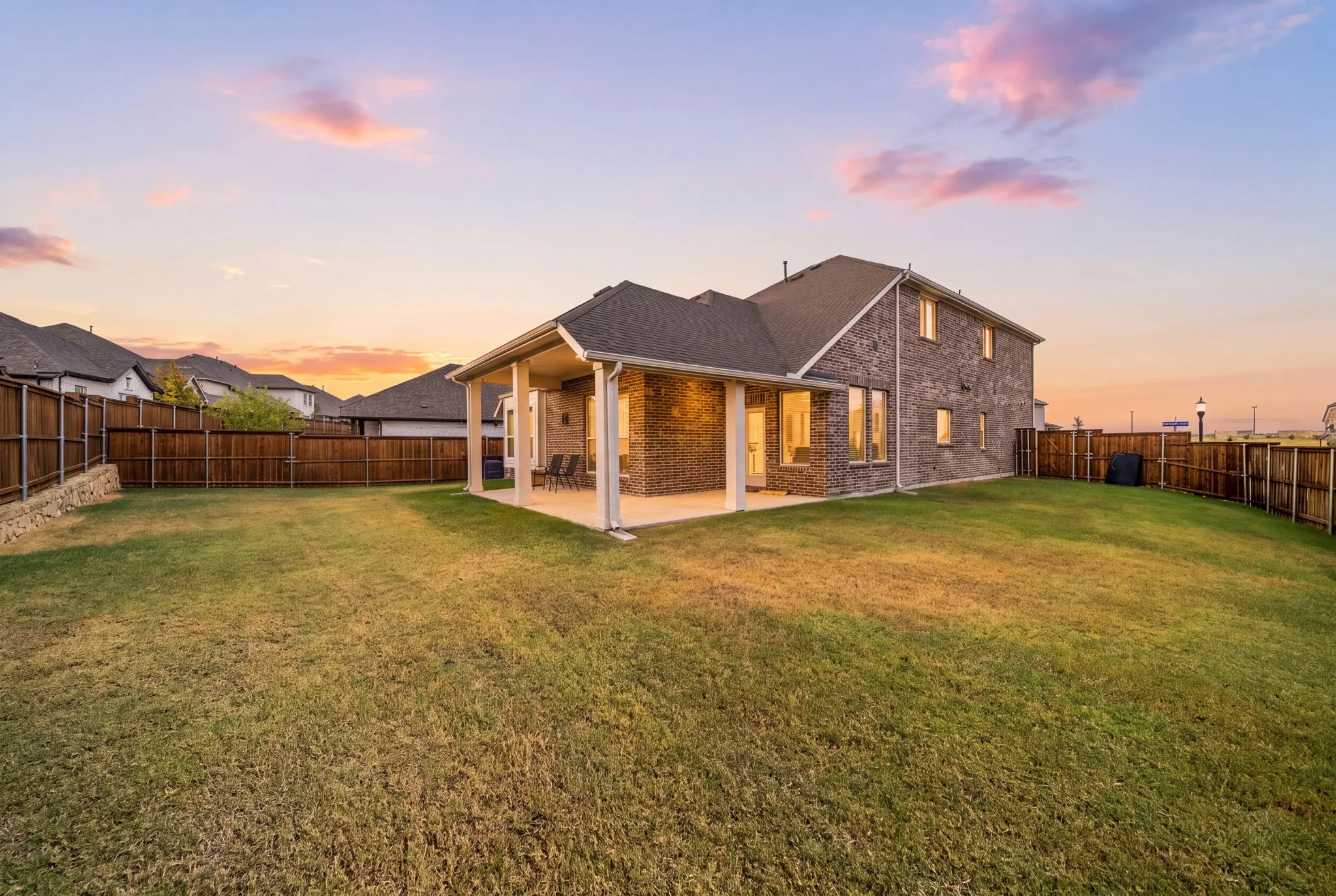 Expansive lawn area with a covered patio, brick exterior, and a privacy fence
