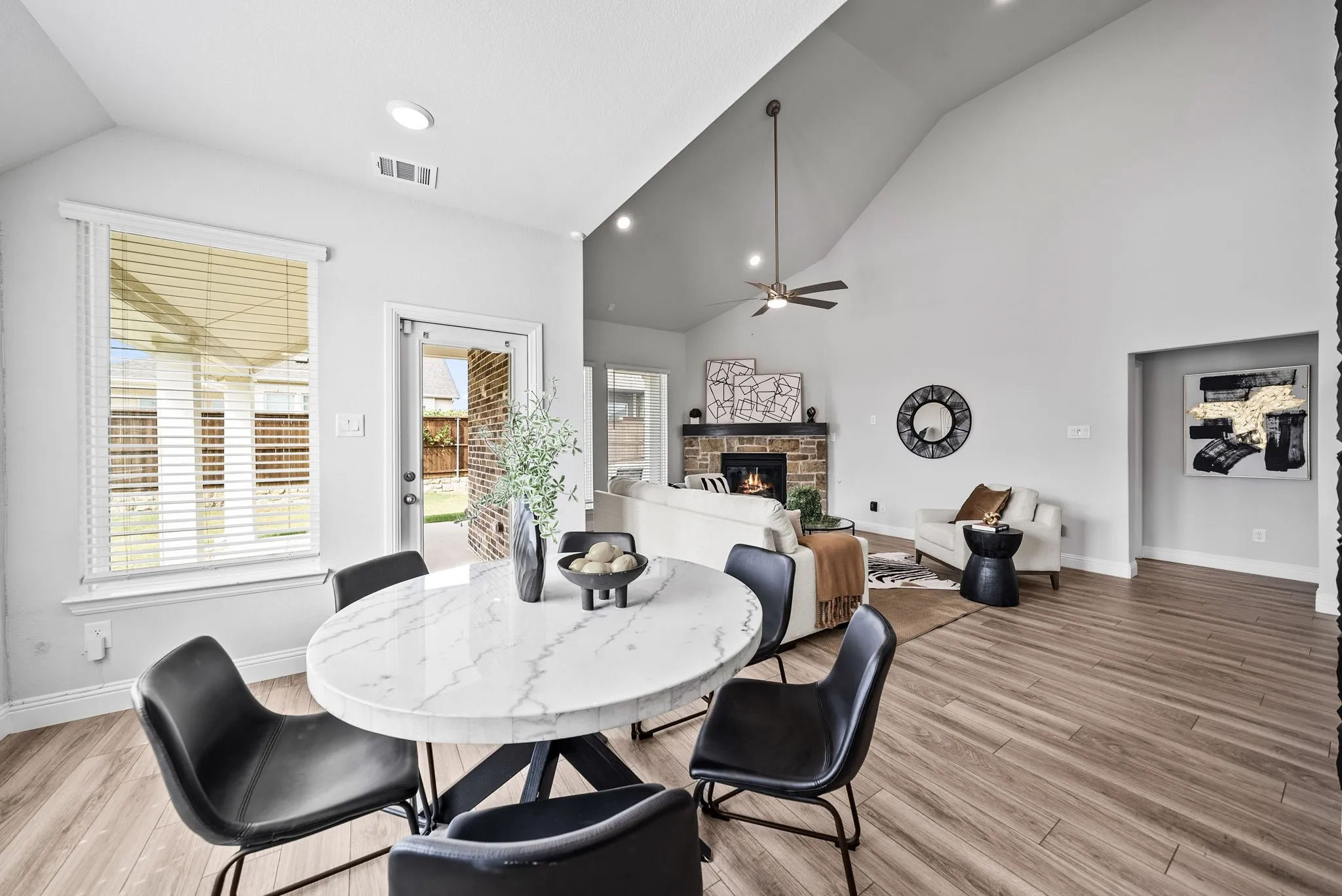 Vaulted ceiling with a ceiling fan, brick fireplace, wood-finish flooring, and white interior walls