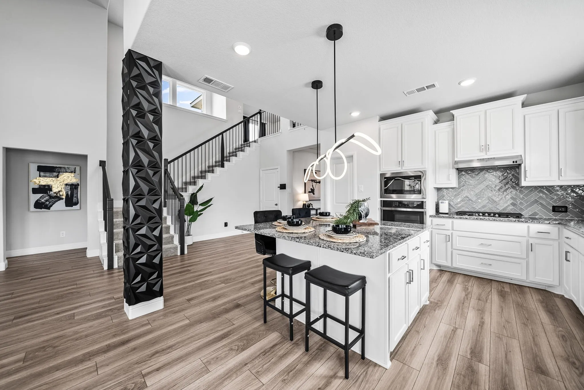 Kitchen island with a granite countertop, wood-finish flooring, white cabinetry, integrated stainless steel appliances, and a chevron tile backsplash
