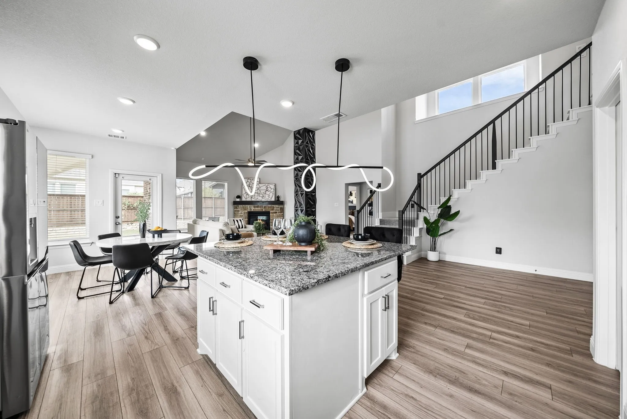 Open-concept living space featuring wood-finish flooring, a kitchen island with stone countertop, and white cabinetry