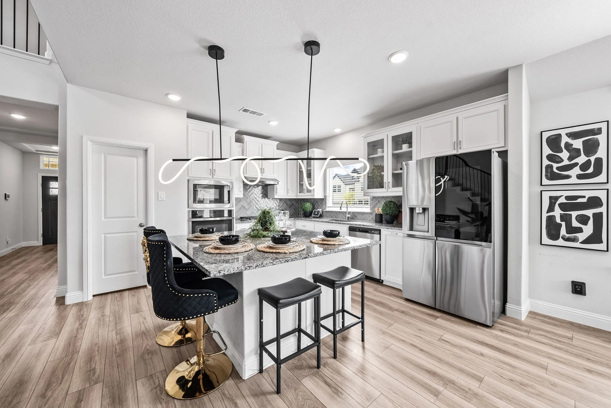 Modern kitchen featuring light wood-finish flooring, white cabinetry, integrated stainless steel appliances, a center island with a stone-finish countertop, and decorative linear pendant lighting