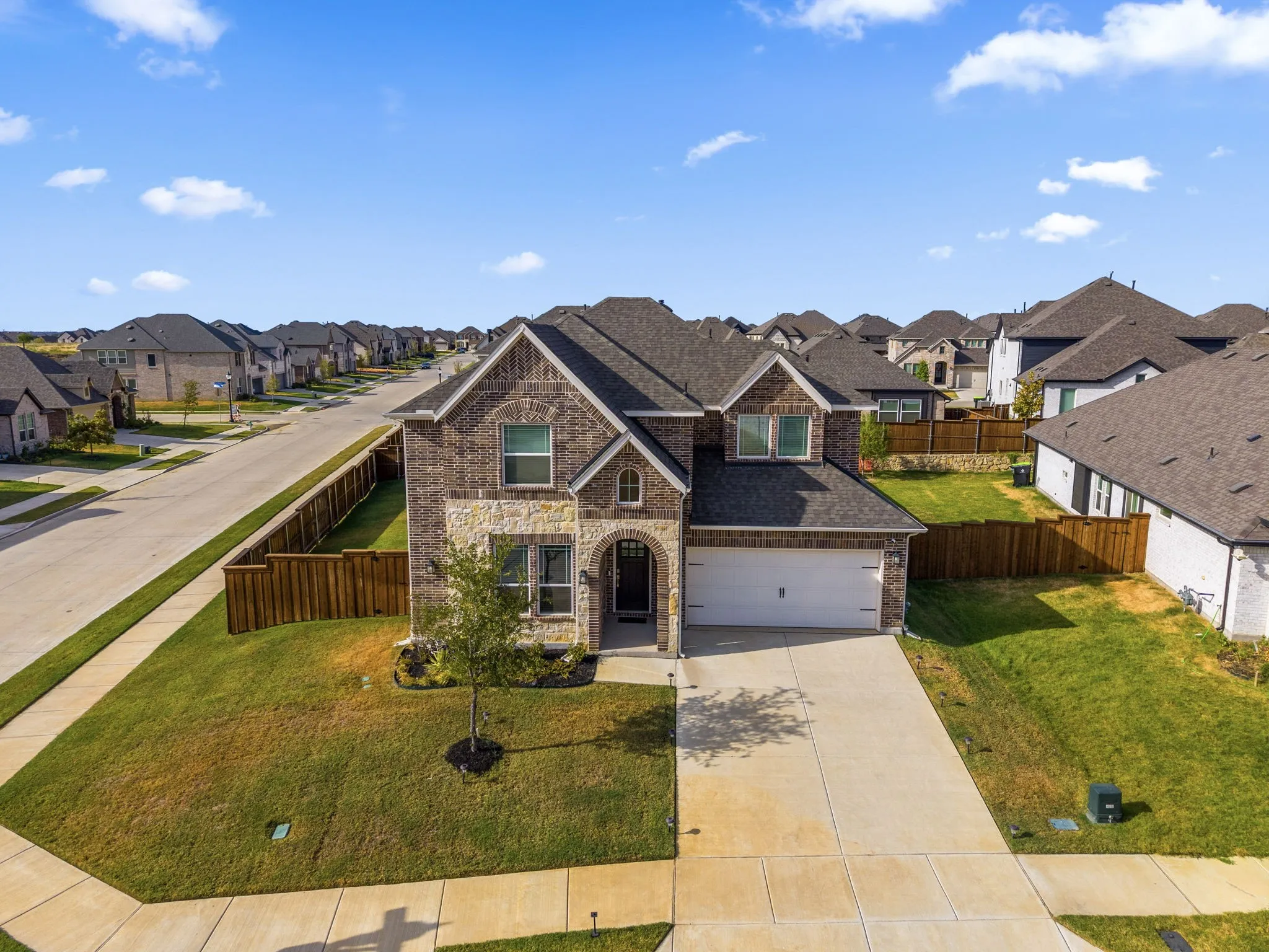 Stunning brick and stone Colonial estate featuring a two-car garage, manicured front lawn with mature landscaping, and a professionally designed exterior elevation