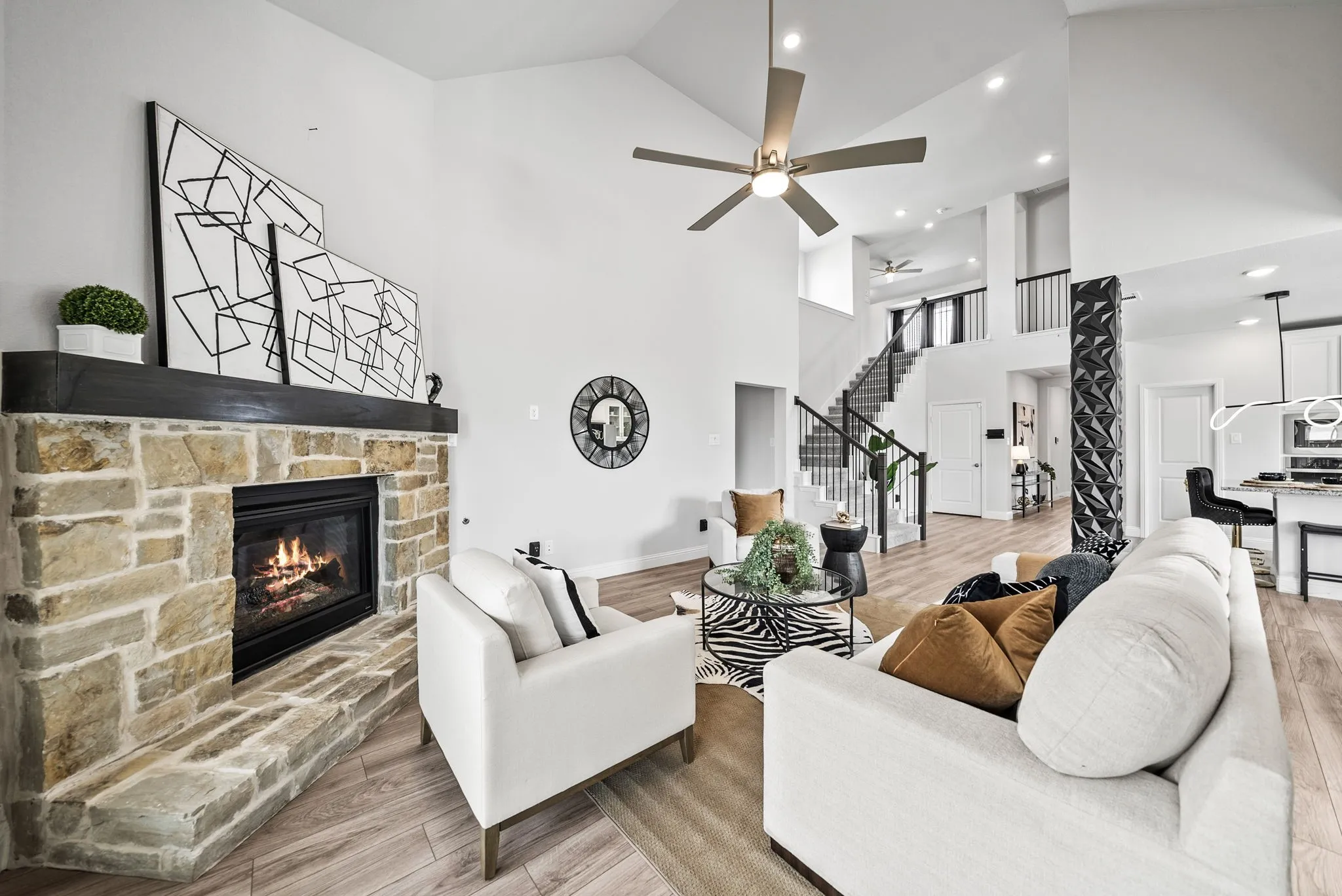 Stone-faced fireplace with a wood mantel, vaulted ceilings, wood-finish flooring, staircase with metal balusters, and a contemporary ceiling fan