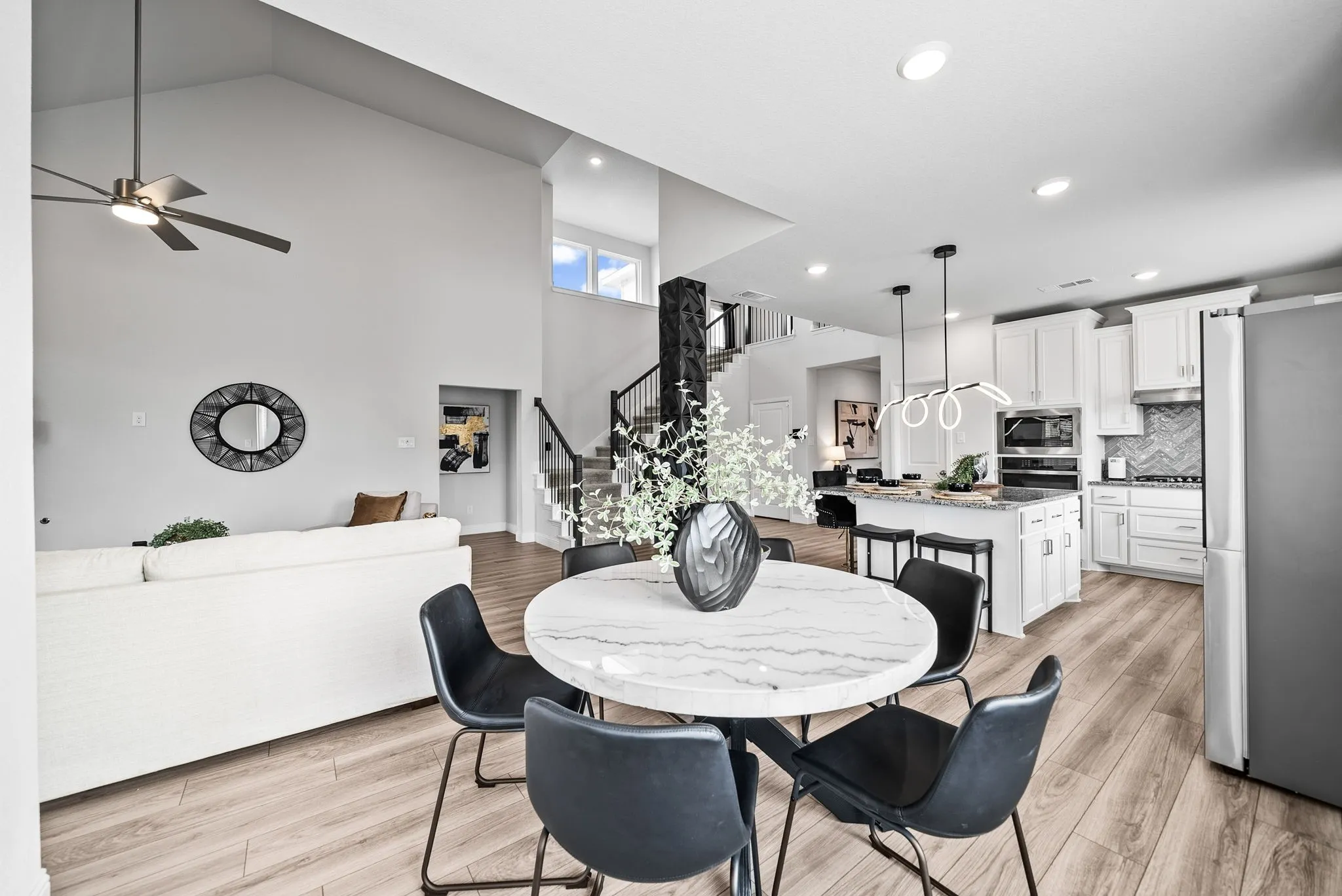 Vaulted ceilings, wood-finish flooring, staircase with metal railings, kitchen island, and white cabinetry