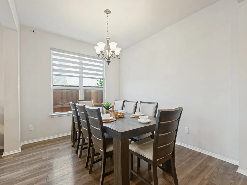 Dining area featuring wood-finish flooring, a contemporary chandelier, and a window with horizontal blinds