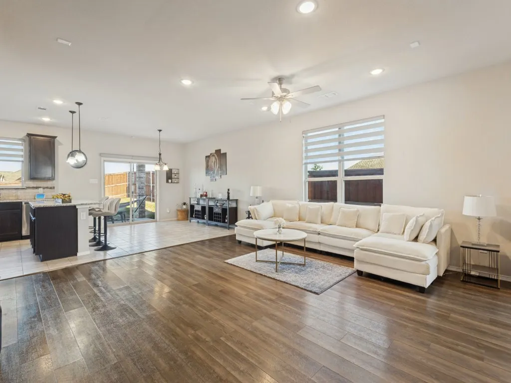 Open-concept living area featuring warm wood-finish flooring throughout, a spacious sectional layout, recessed ceiling lighting, and ceiling fan with integrated light fixture