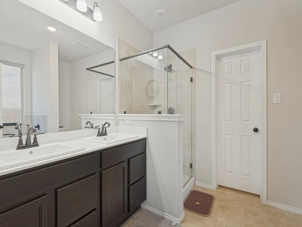 Spa-inspired primary bathroom featuring a dark-finish vanity with dual sinks, white quartz countertops, and polished chrome faucetry