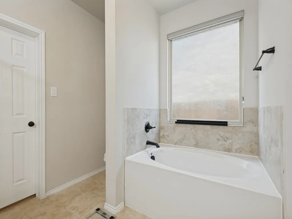 Soaking tub with black fixtures, tiled surround, and a frosted window