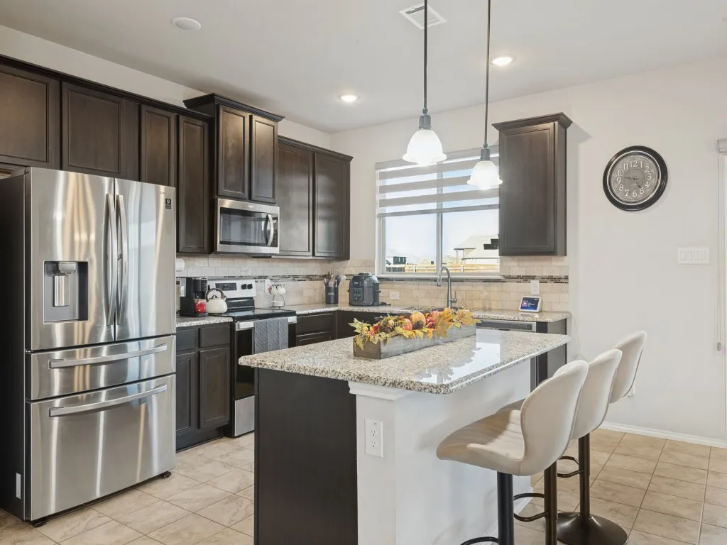 Kitchen featuring dark wood-finish cabinetry, stainless steel appliances, granite countertops, an undermount sink, and a tiled backsplash