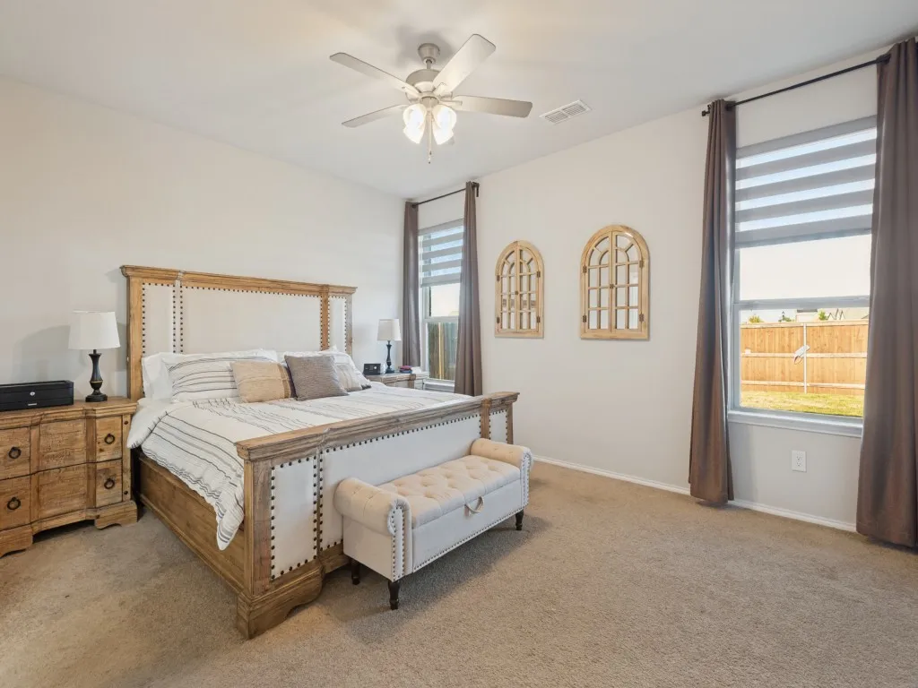 Carpeted flooring, ceiling fan with integrated lighting, two large windows, and a neutral color palette