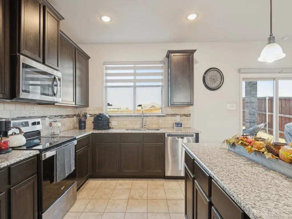 Modern kitchen featuring dark wood cabinetry, stainless steel appliances, and granite countertops with waterfall edge