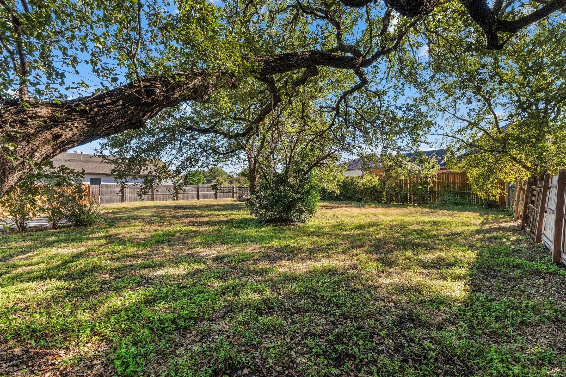 Expansive backyard with mature shade trees and lush lawn, bordered by wooden fencing