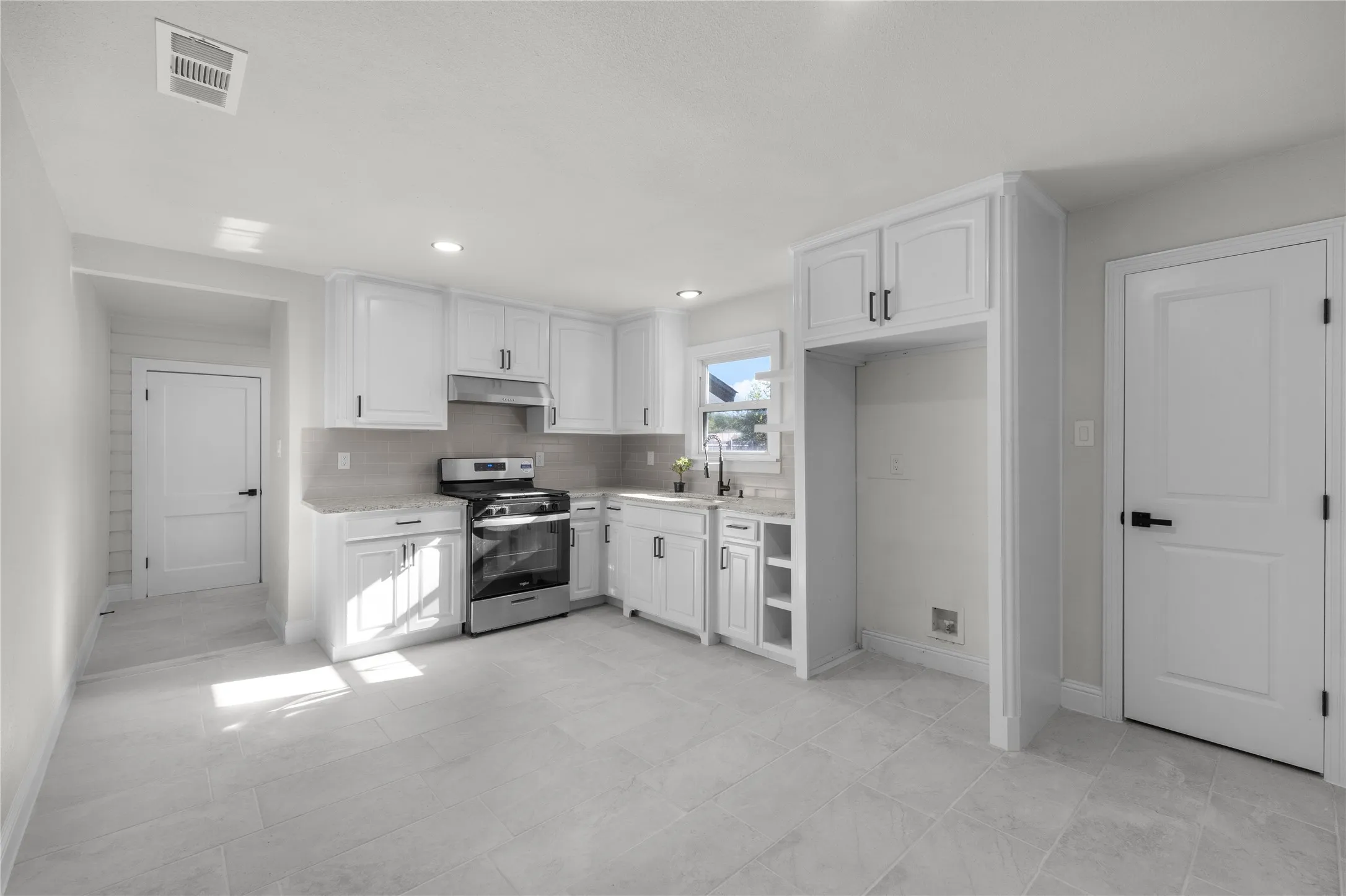 Modern kitchen featuring white shaker cabinetry, stainless steel range, light-toned tiled flooring, and recessed lighting