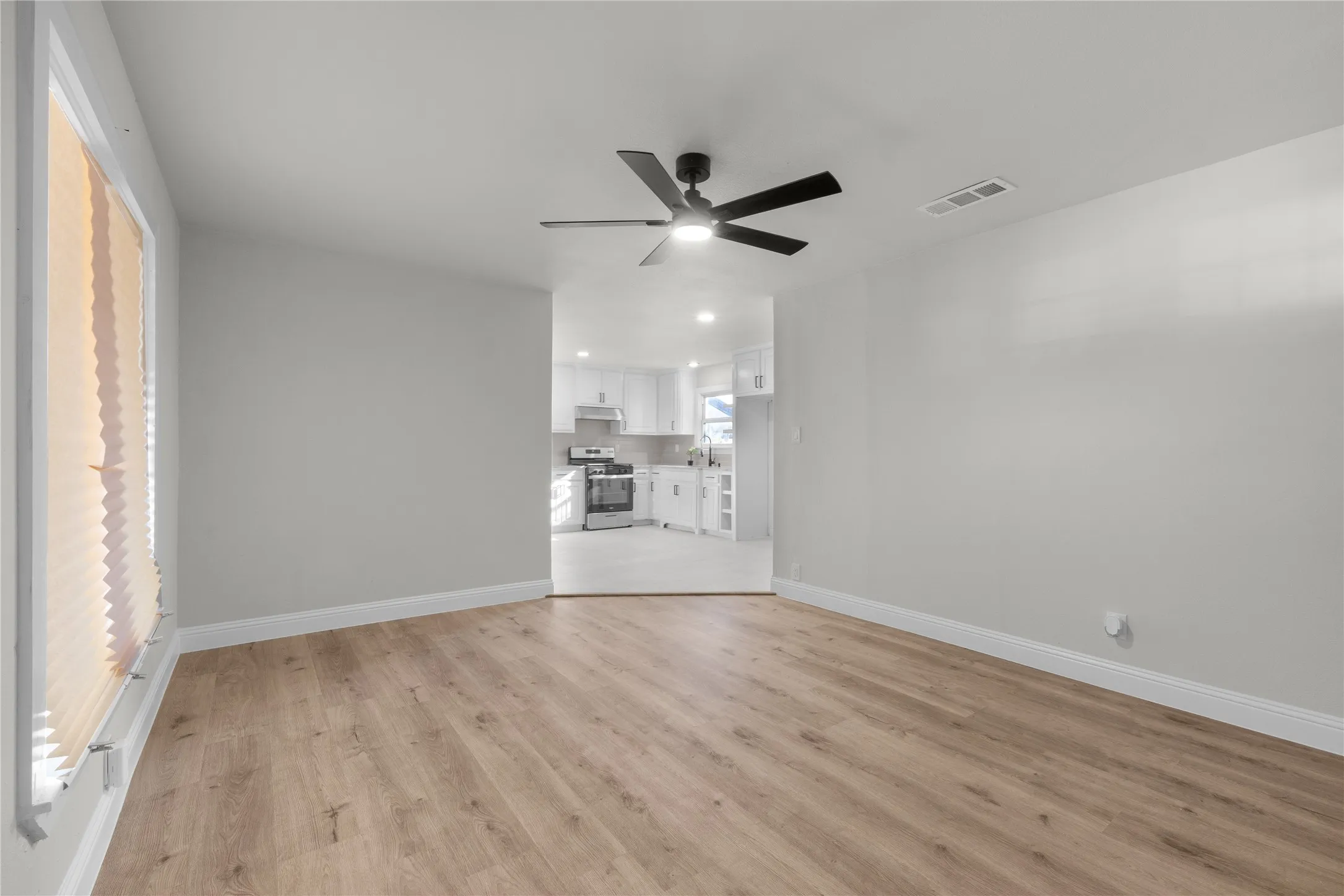 Spacious open living area featuring wood-finish flooring, neutral wall finishes, and a ceiling fan with integrated lighting