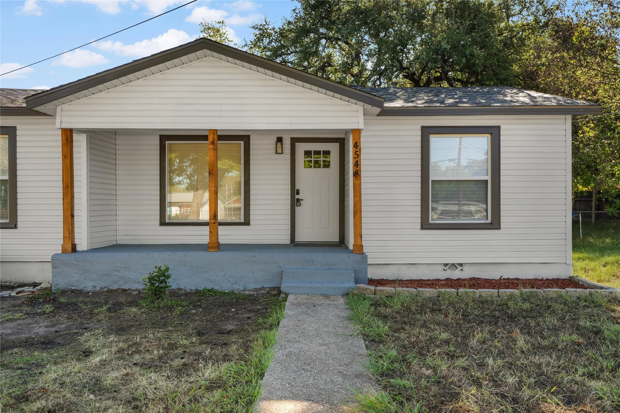 Charming cottage-style home featuring a covered front porch with wood-trimmed support posts, large picture window, and contemporary white fiber cement siding