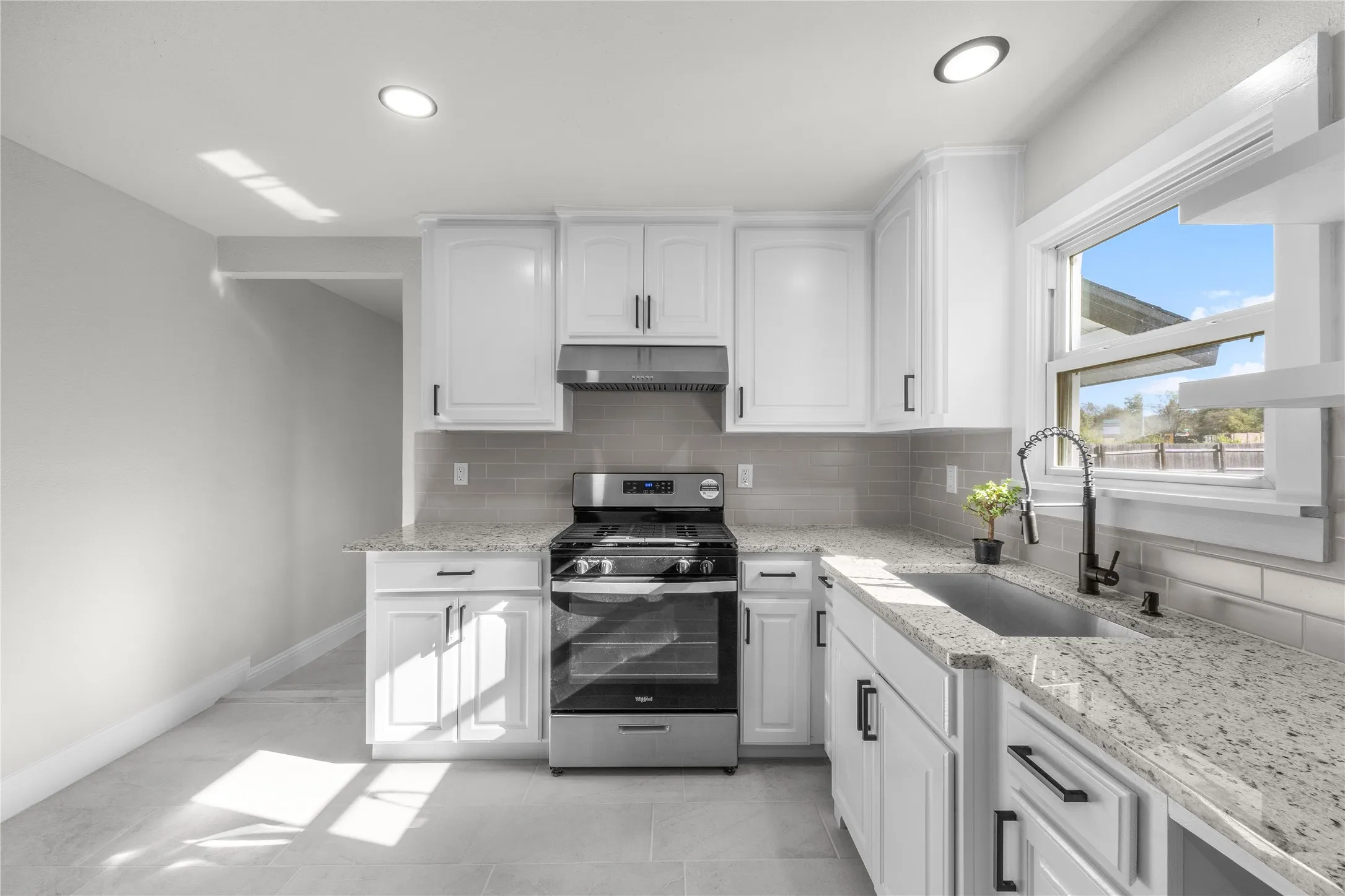 White cabinetry with black hardware, stainless steel appliances, light-toned countertop, subway tile backsplash, and recessed lighting