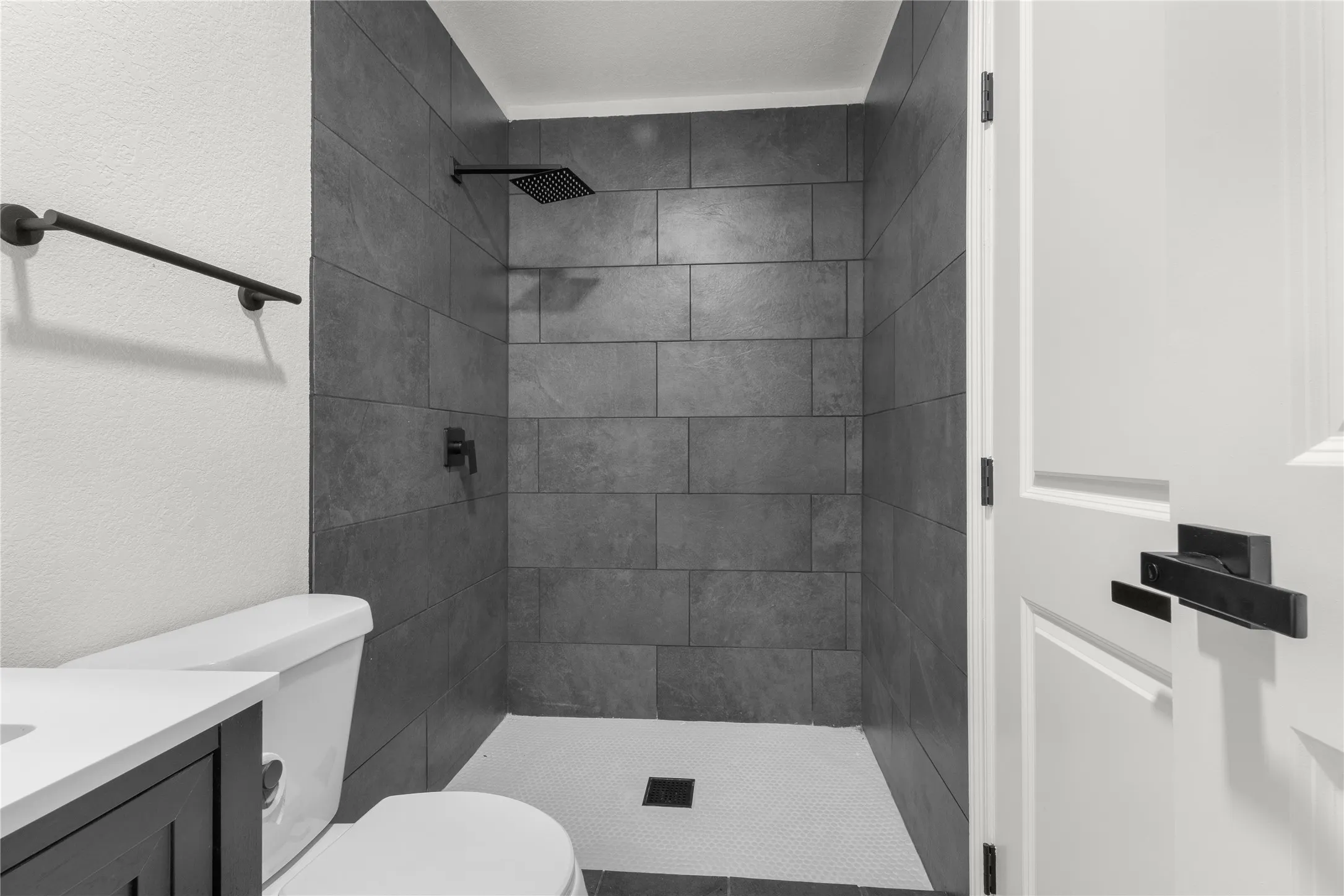 Shower featuring grey tile surround, matte black rainfall shower head, and matte black fixtures