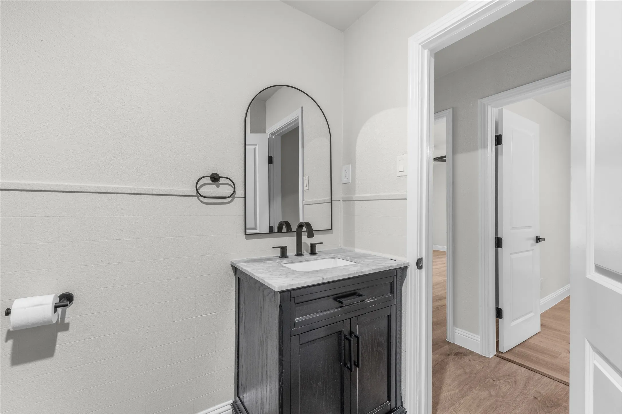Dark wood-finish vanity with a light countertop, black hardware, and an arched mirror