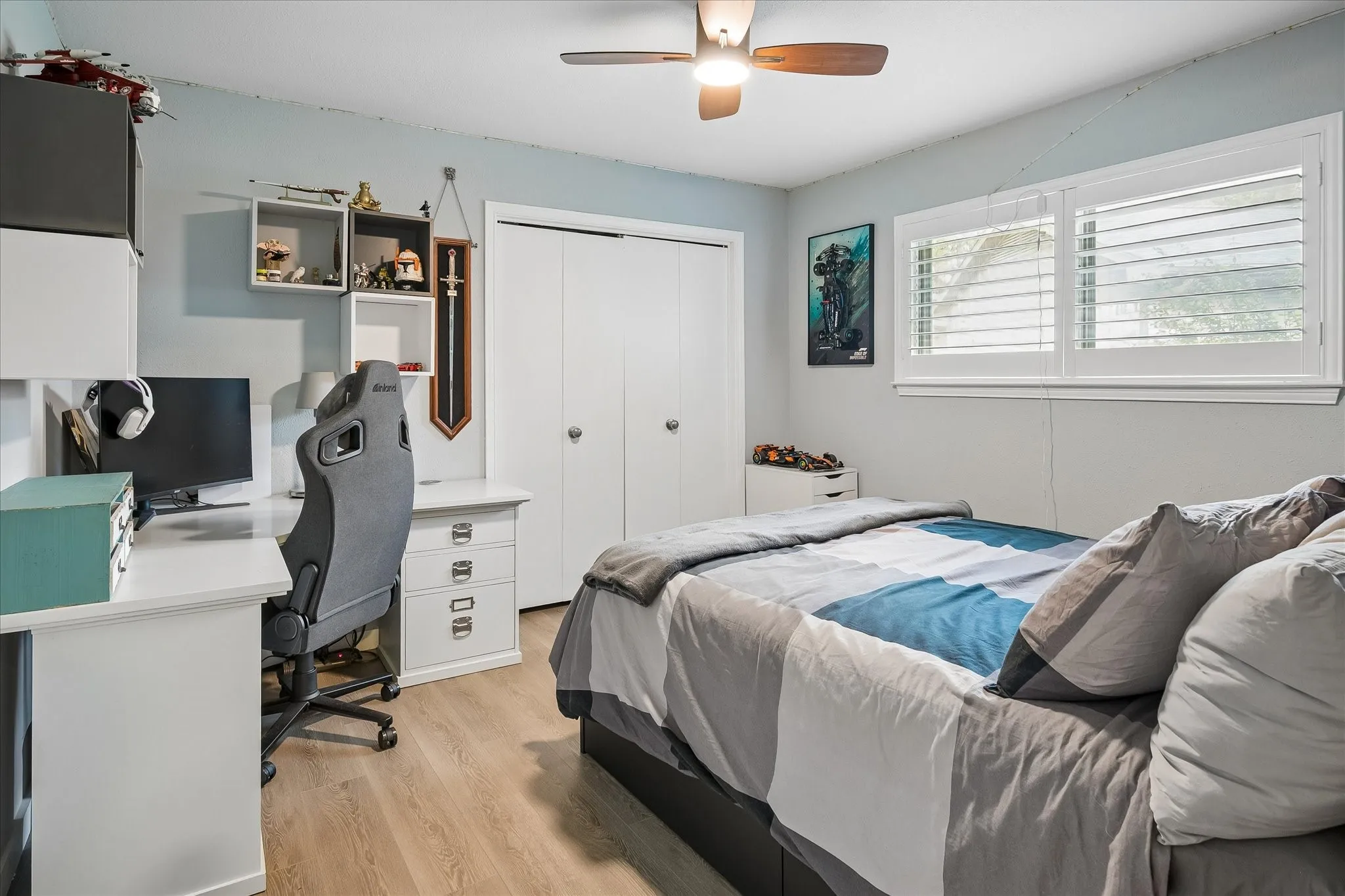 Light-filled room featuring wood-finish flooring, a ceiling fan with integrated lighting, dual-panel closet doors, and plantation shutters
