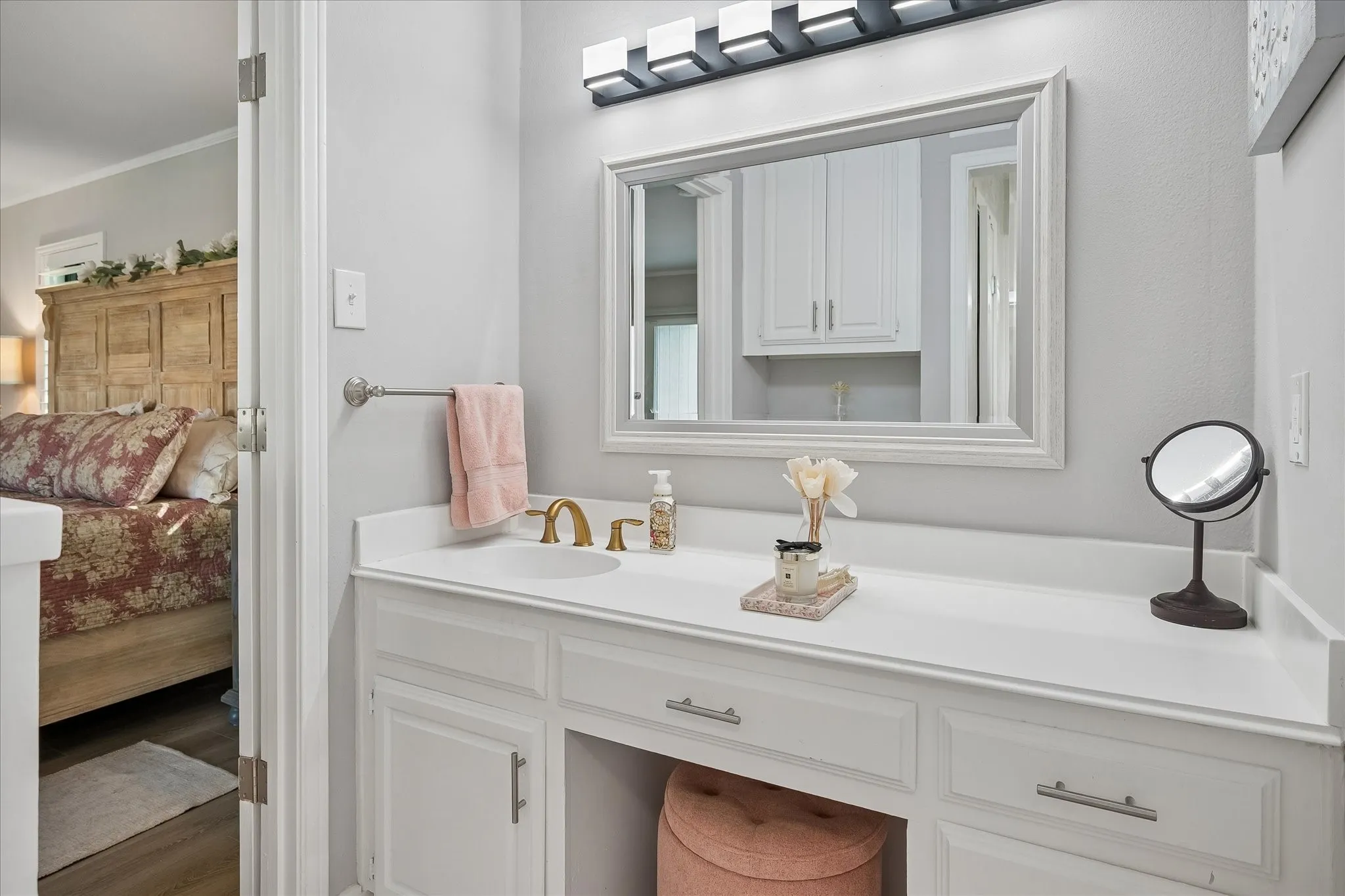 White built-in vanity featuring a solid surface countertop, integrated sink, brass-tone faucet hardware, and a framed mirror with integrated four-light fixture
