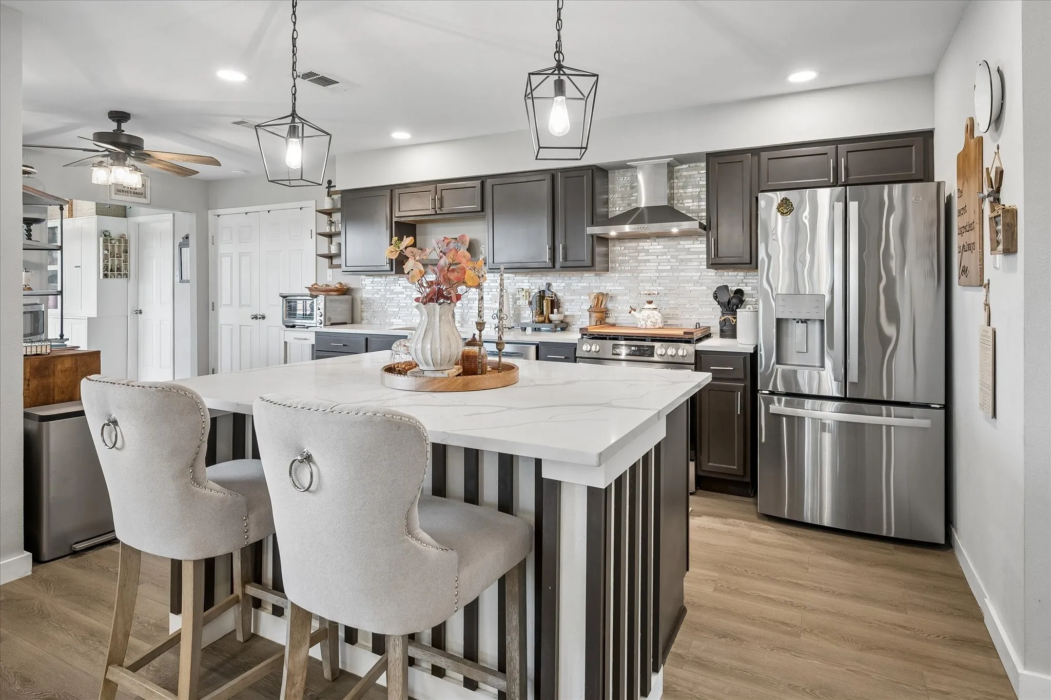 Kitchen featuring dark wood cabinetry, a central island with a white stone-surface countertop, stainless steel appliances, a tile backsplash, and wood-finish flooring